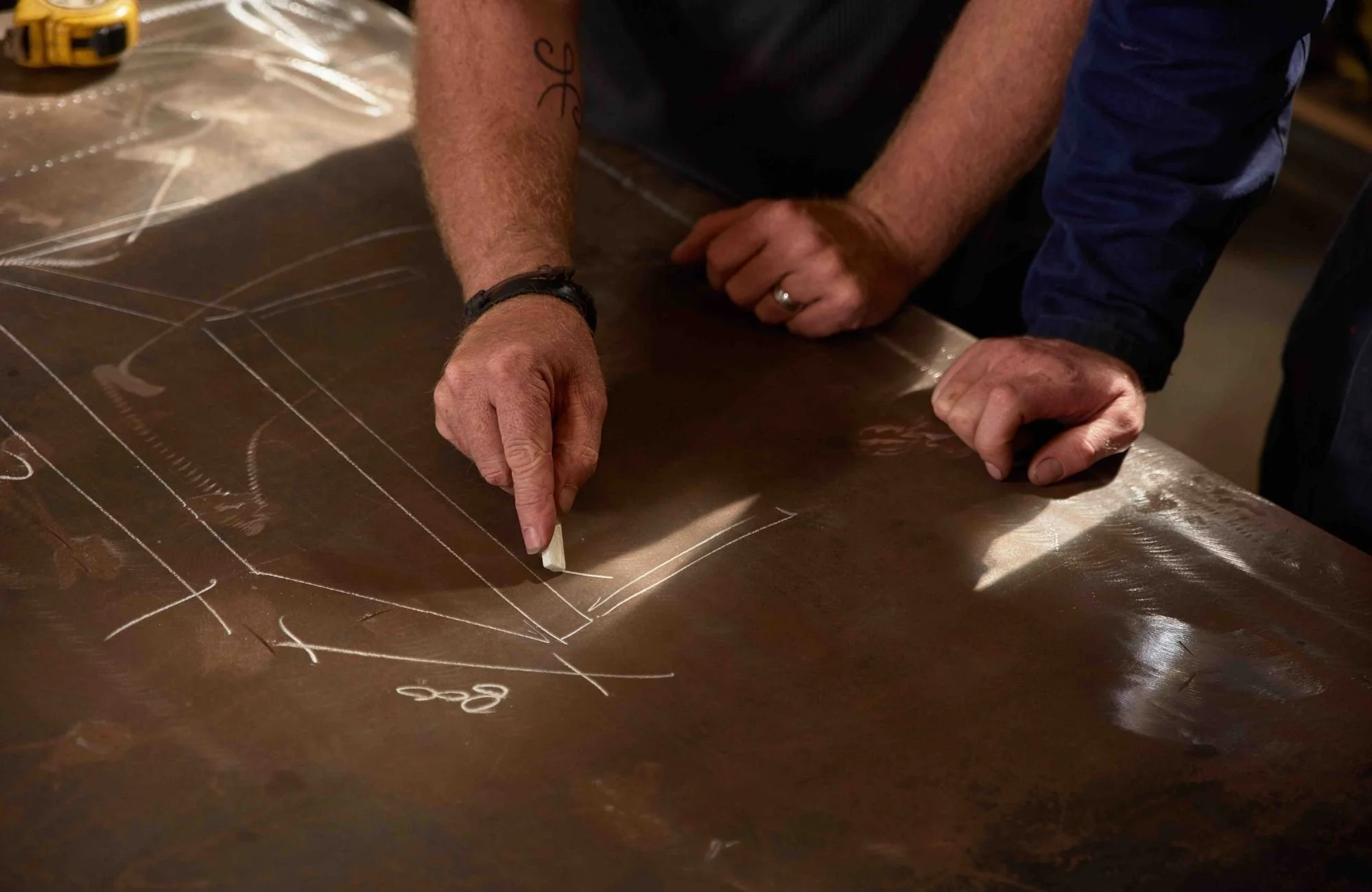 a fabricator drawing a design with chalk on a board