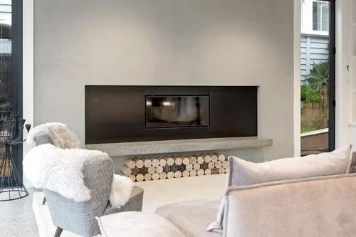 A fireplace with steel panel surround within a middle of a minimalist style lounge of a house in Ponsonby.
