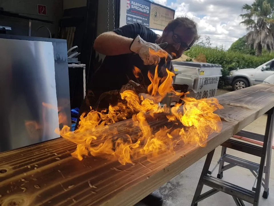 A fabricator working with flames to create an aged timber effect