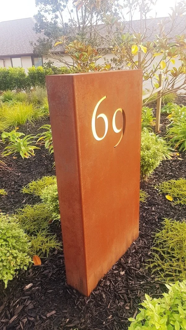 a tall corten steel letterbox in a garden setting - Wainui