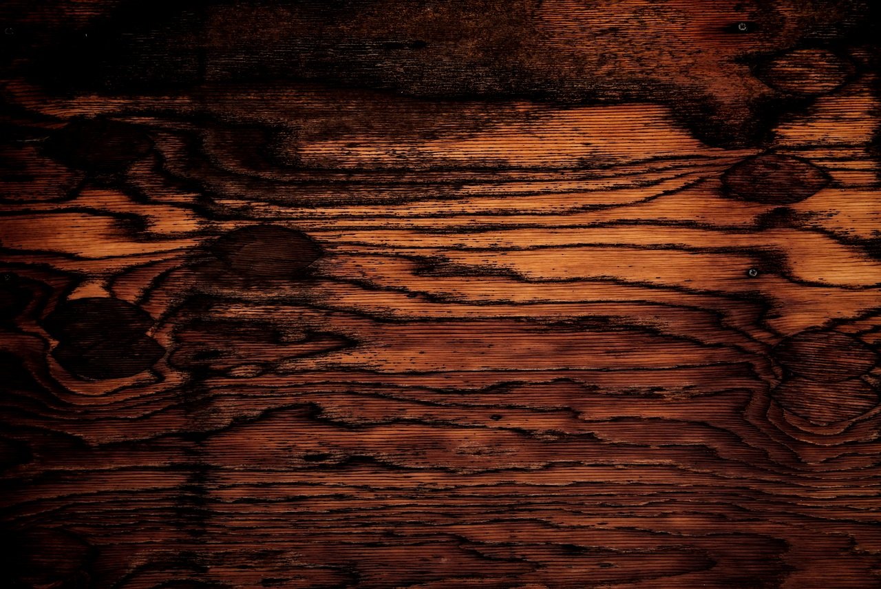 Raw Possessions logo - a close-up of a dark stained wooden surface with visible wood grain and knots.