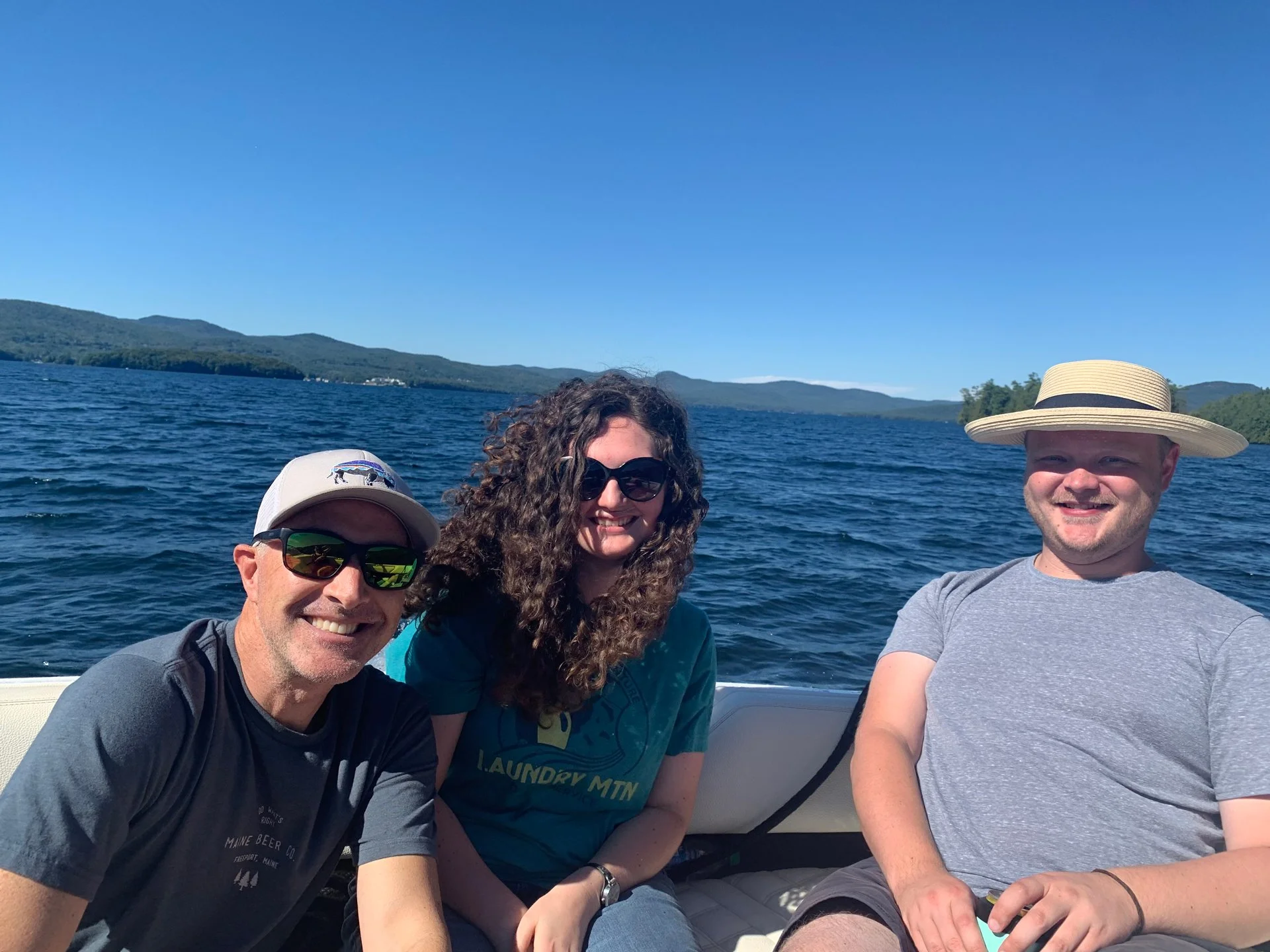 Four people smiling on a boat with a lake and mountain landscape in the background.