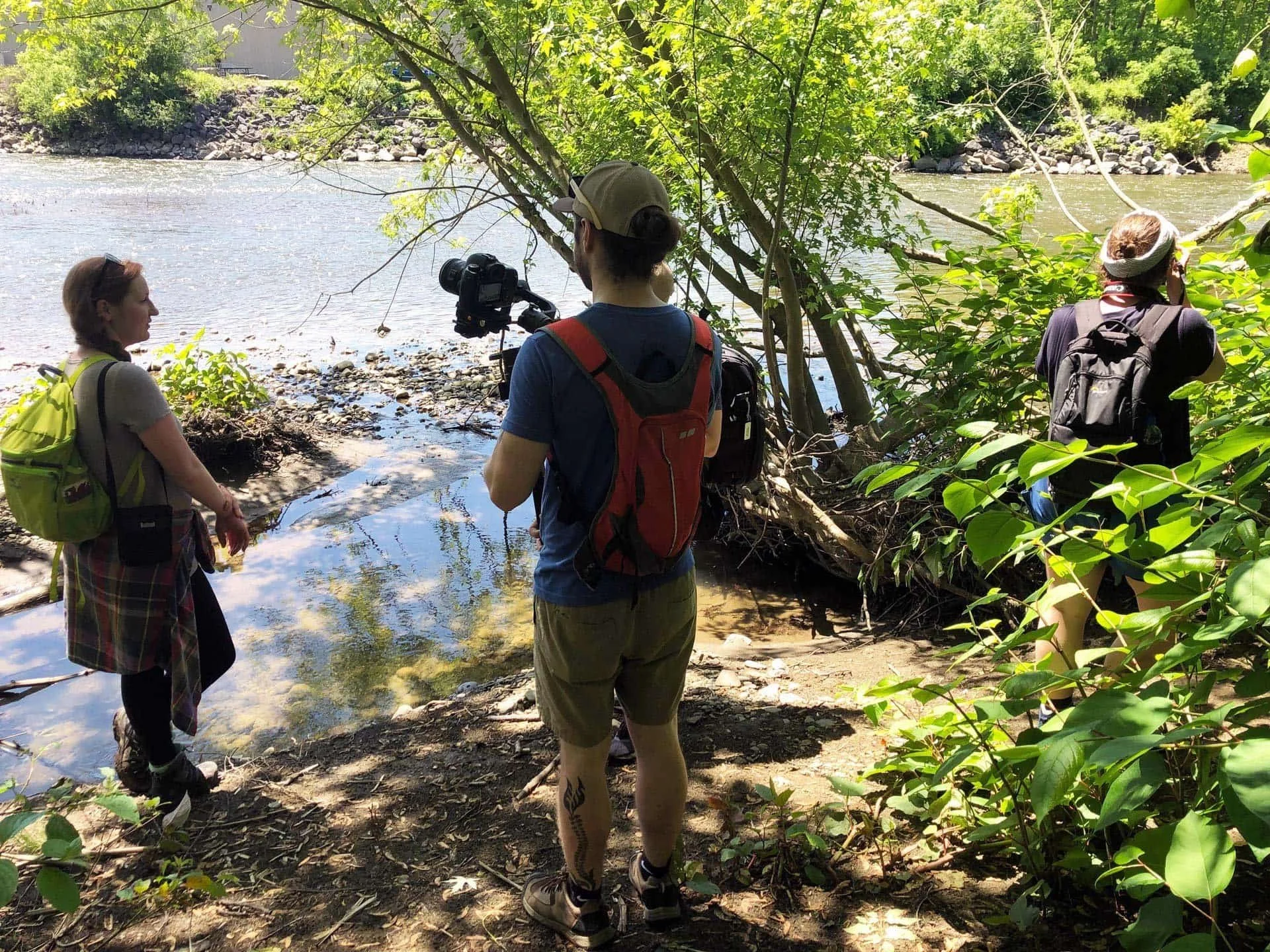 Three photographers take photos along a river bank.