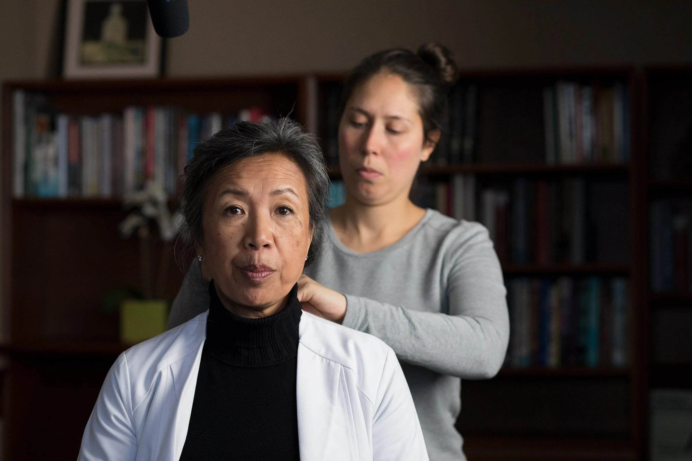 A crew person places a microphone on a woman in a lab coat.