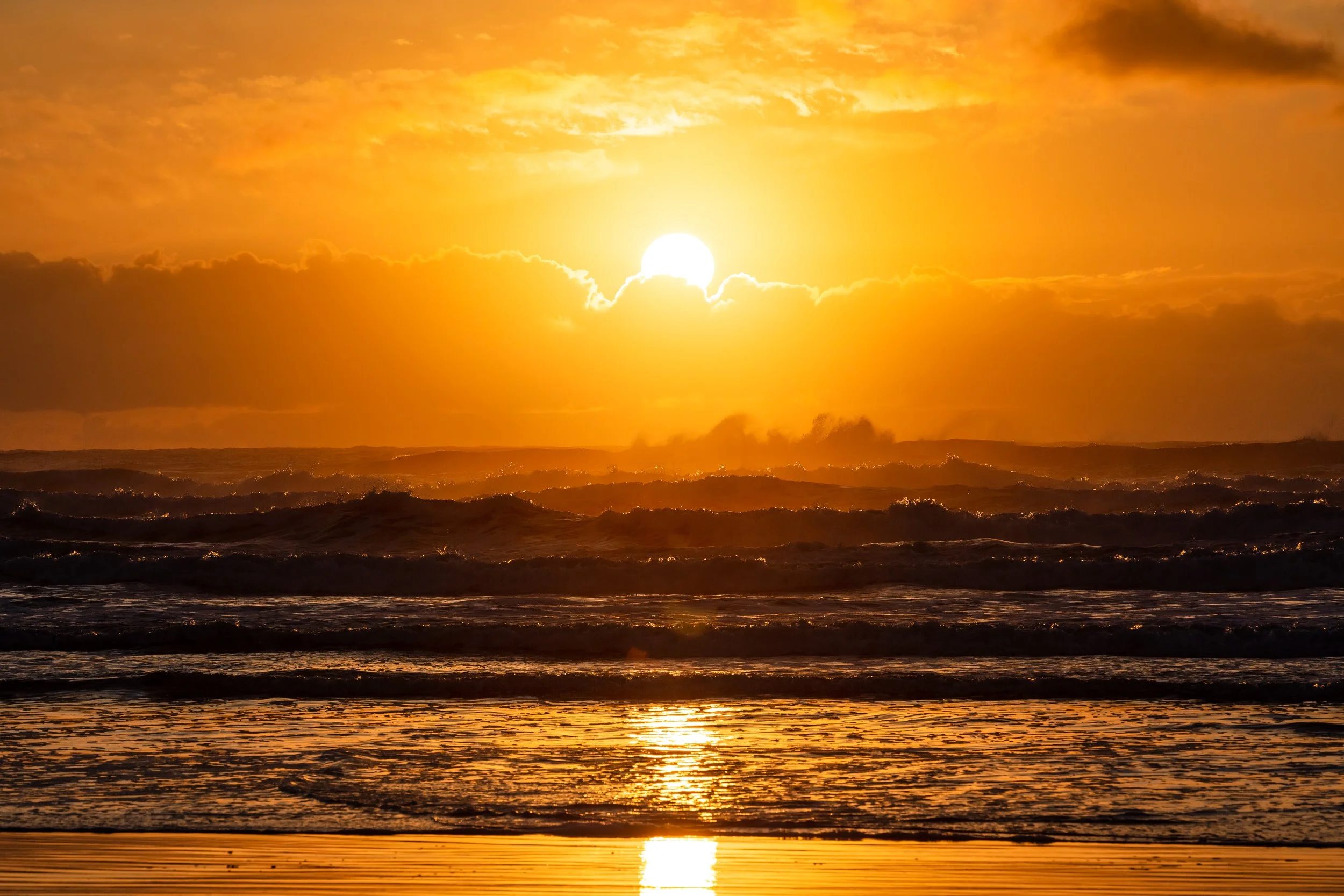 Sunset over the ocean with waves and reflections on the wet sand