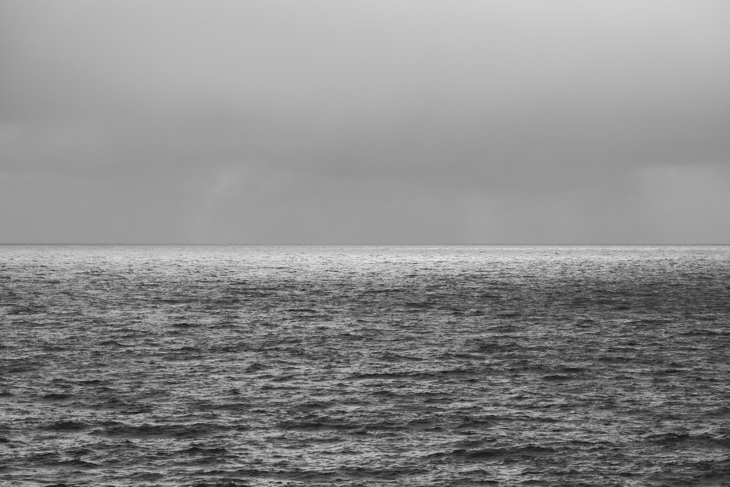 Black and white photo of calm ocean waves with a cloudy sky.