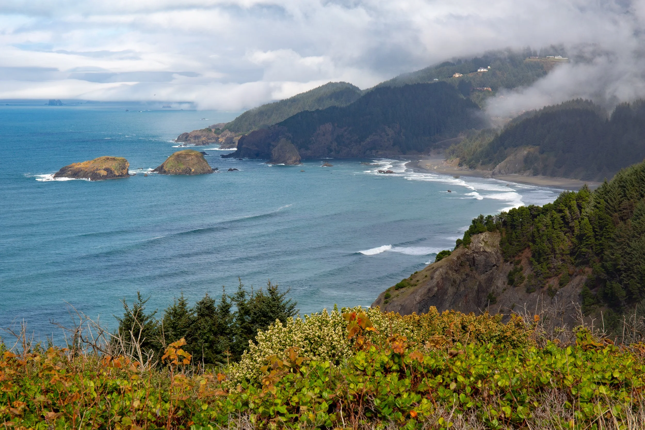 Scenic view of a rugged coastline with rocky islands, green cliffs, and the ocean under a cloudy sky.