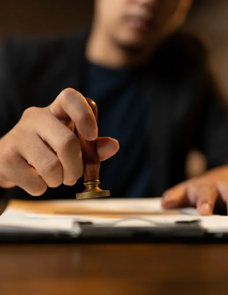 A person holding a stamp and pressing it onto a document on a desk.