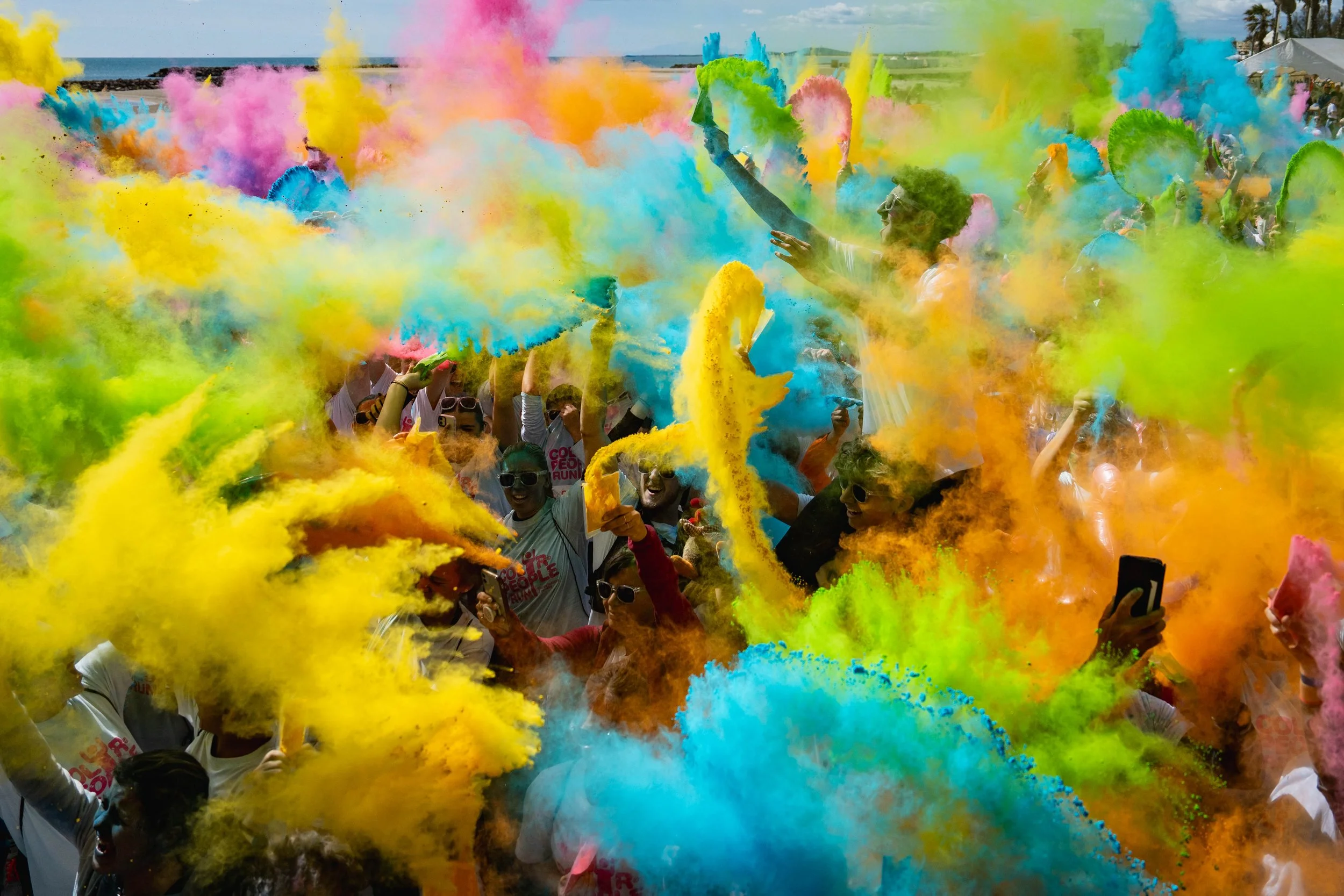 Groupe de personnes participant à une fête de couleur avec des nuages de poudre colorée en rouge, jaune, vert, bleu et rose lors d'un événement en plein air.