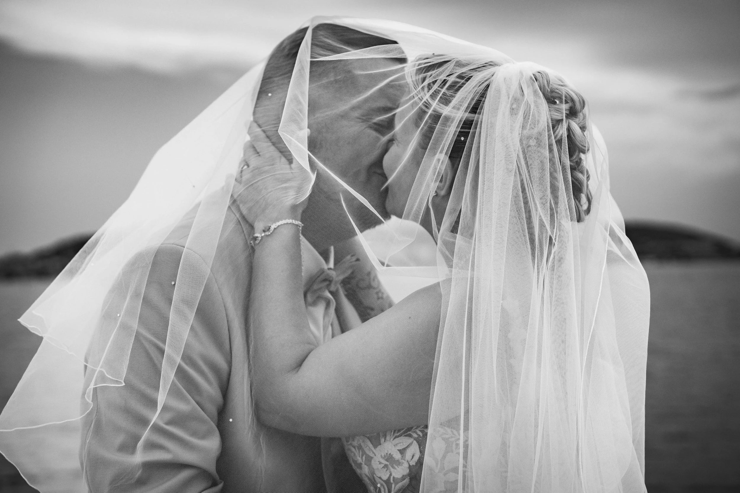 Un couple de marié danse sous un voile blanc d'une robe de mariage avec Sète en arrière plan, scène romantique en noir et blanc.