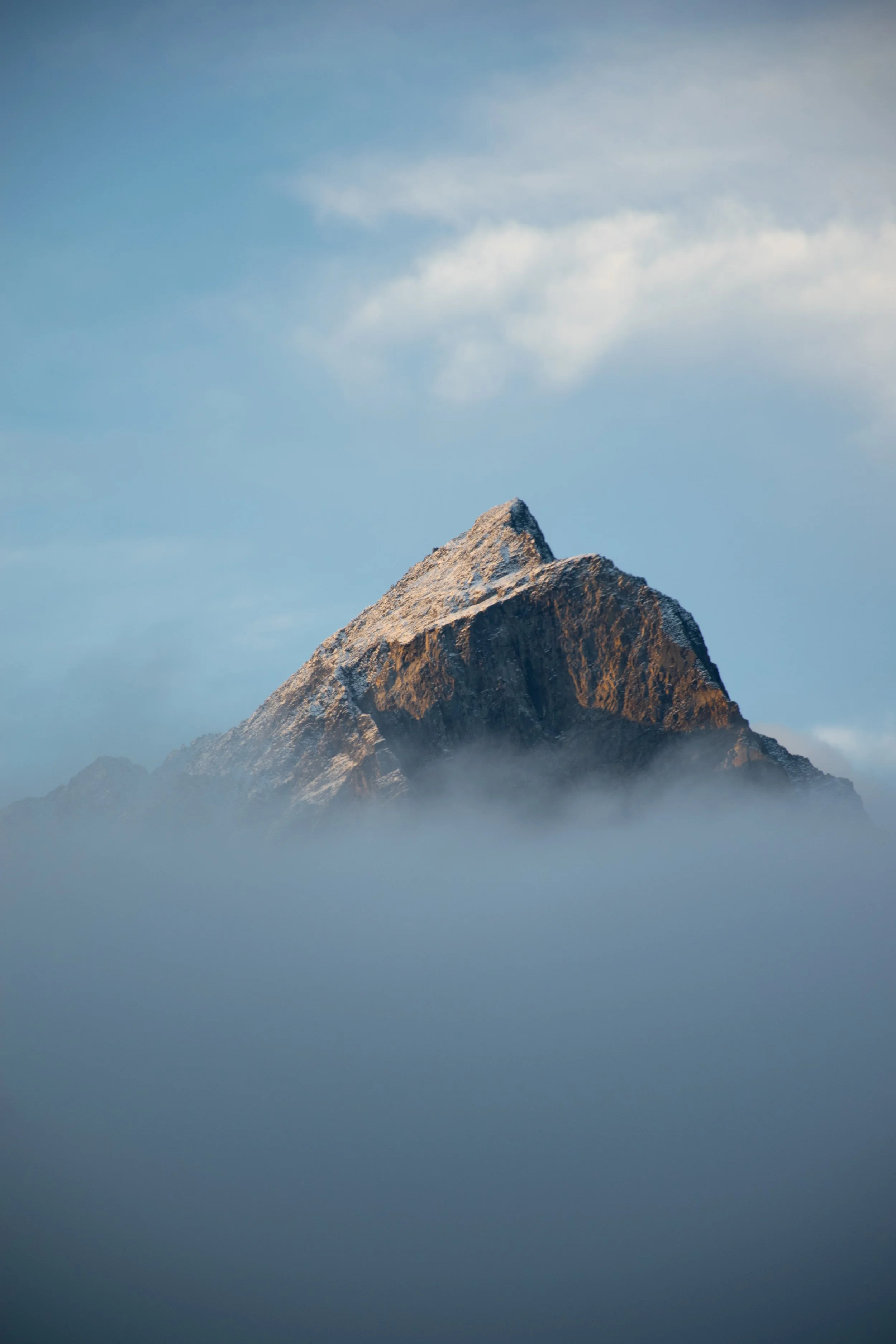 A mountain peak emerging through clouds with a bright blue sky in the background.