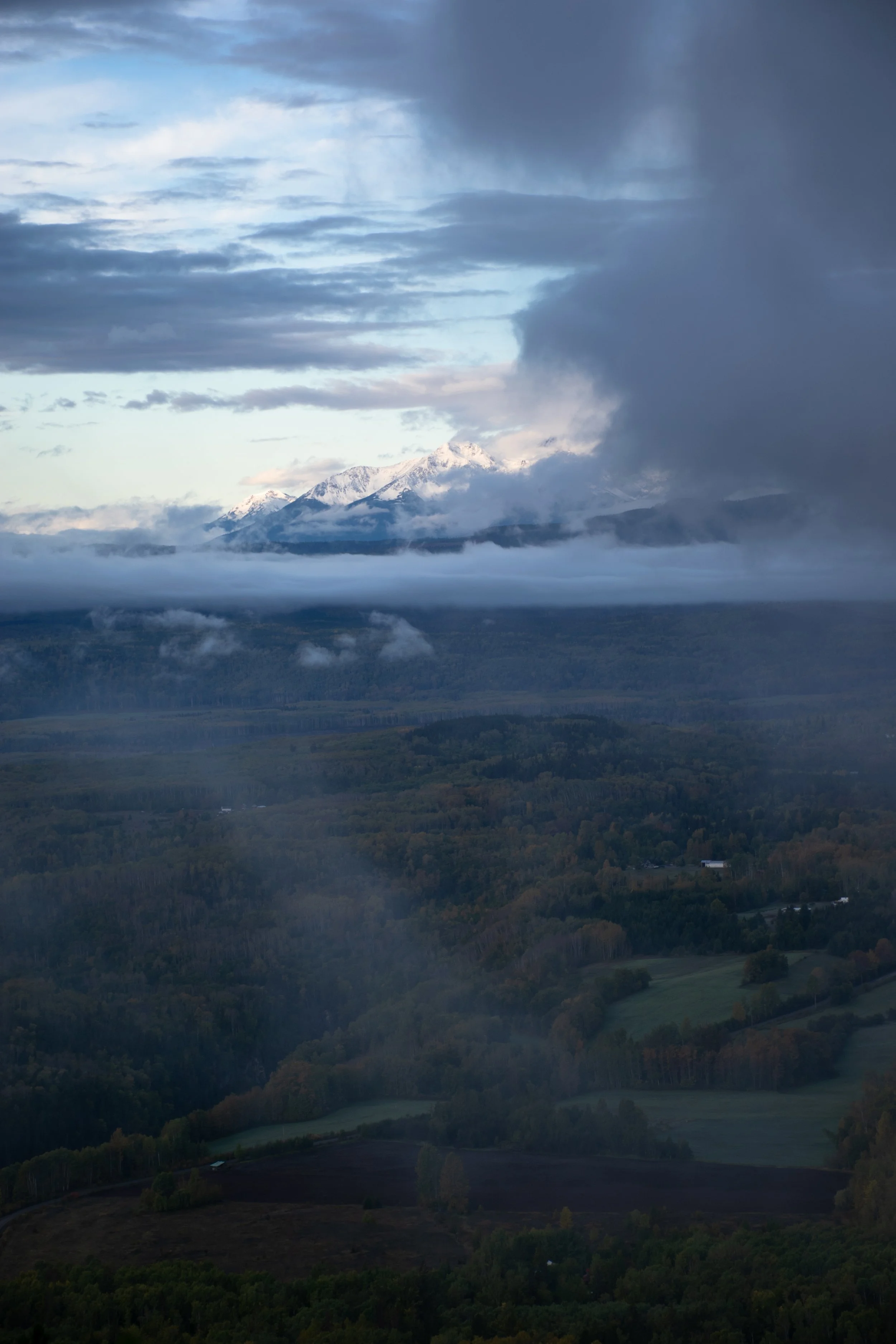 Snow-capped mountains with partly cloudy sky and fog in a green landscape.
