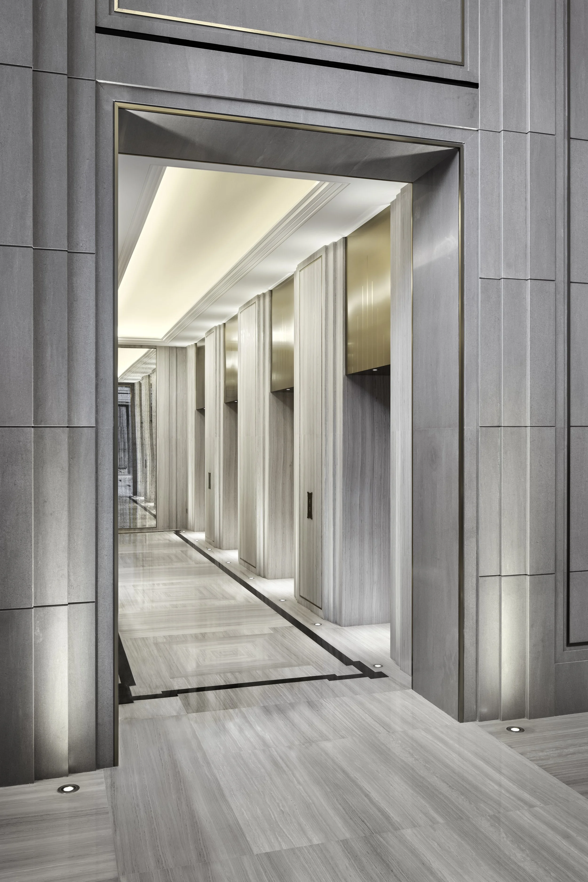 Interior view of a modern elevator lobby with marble flooring, vertical wood wall panels, and a ceiling with recessed lighting.