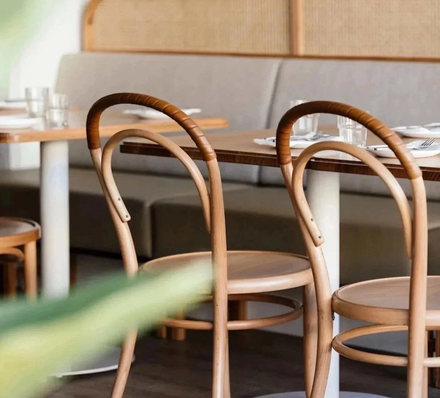 Wooden chairs with curved backs around a dining table set with plates, glasses, and utensils in a restaurant or cafe.