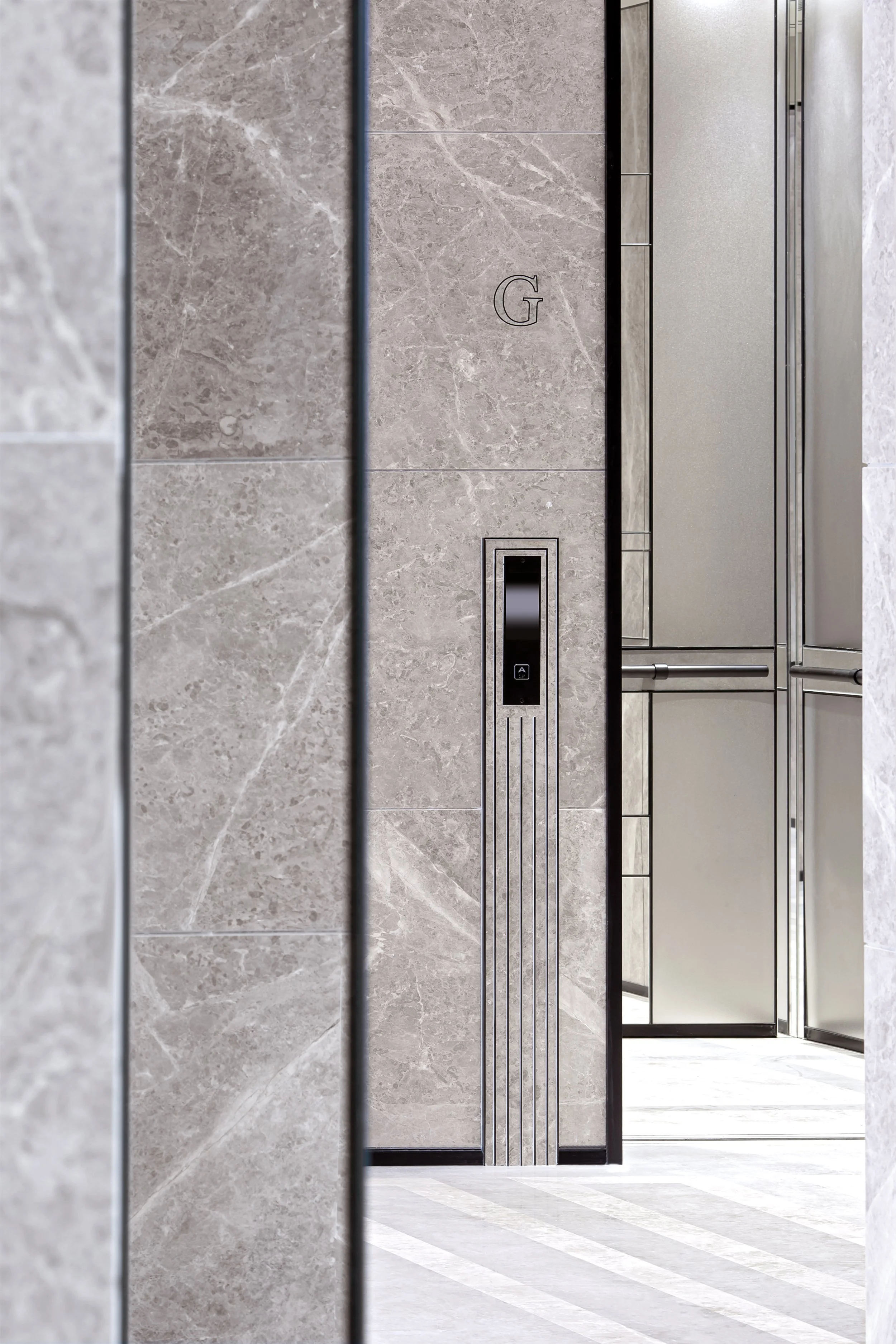 Inside an elevator with gray marble walls, black metal accents, and a control panel. The elevator door is open, revealing a tiled floor with diagonal light and dark gray stripes.