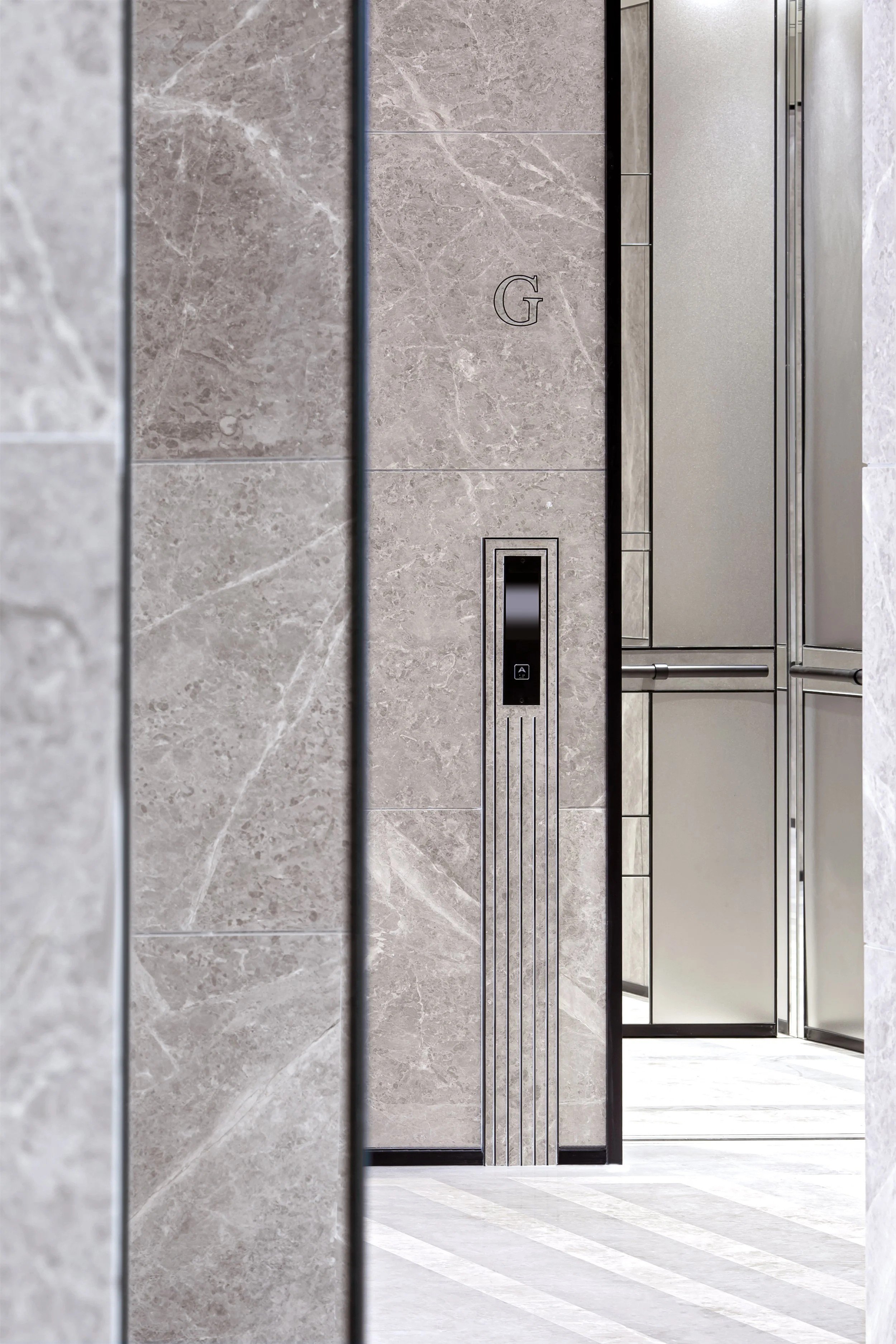 Elevator door in a modern building with a gray marble wall and a striped pattern on the floor.