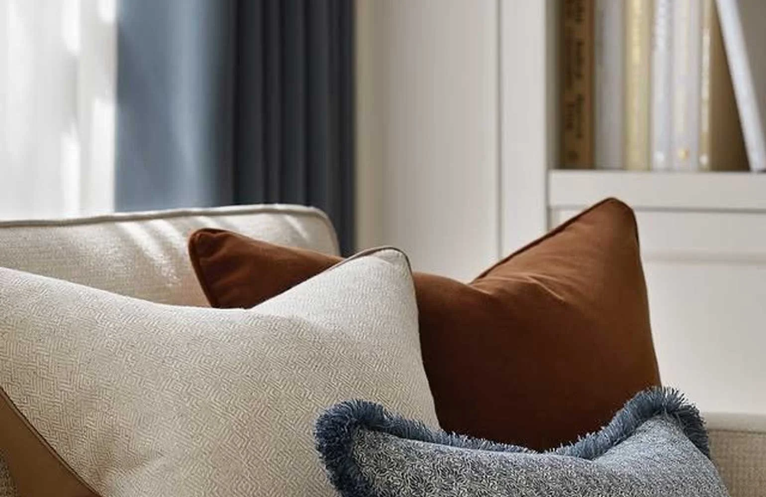 Close-up of beige, brown, and gray decorative pillows on a sofa in a cozy living room.