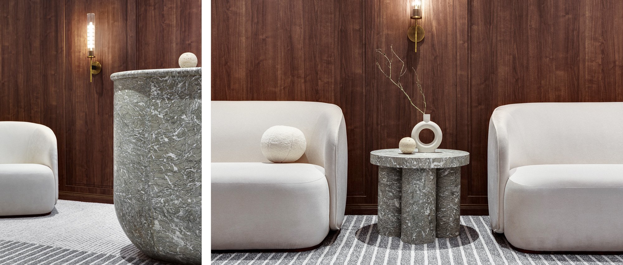 Modern interior with white sofas, round marble side tables, a wooden wall with brass wall sconces, and minimalist decor including vases and a branch in a vase.