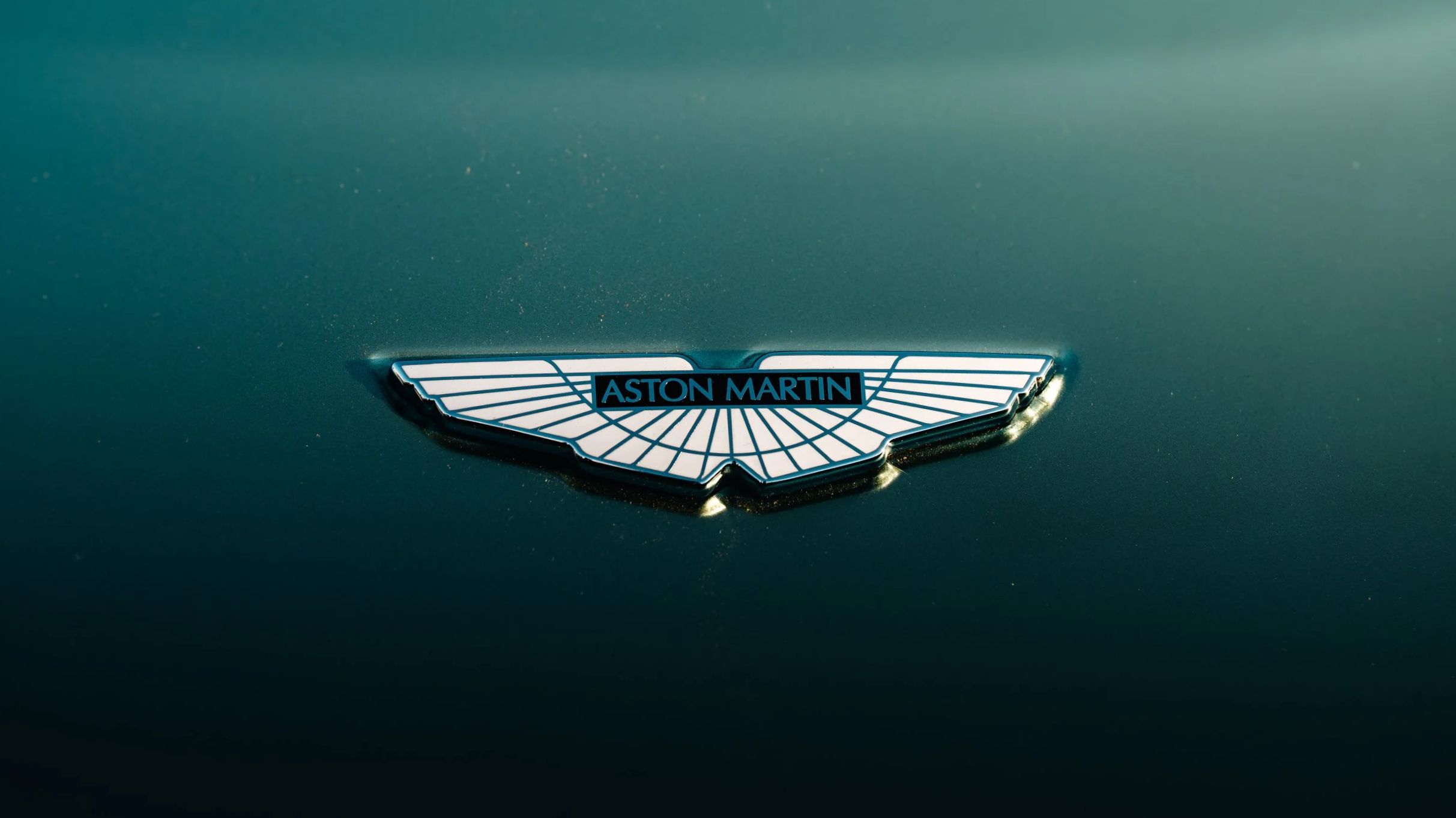 Close-up of an Aston Martin emblem on a green car hood.