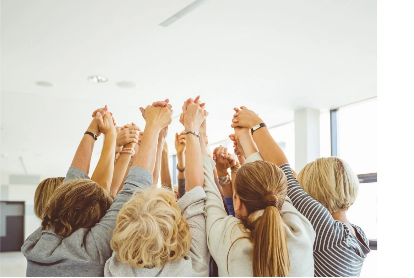 Women standing in a circle holding hangs with their arms in the air.