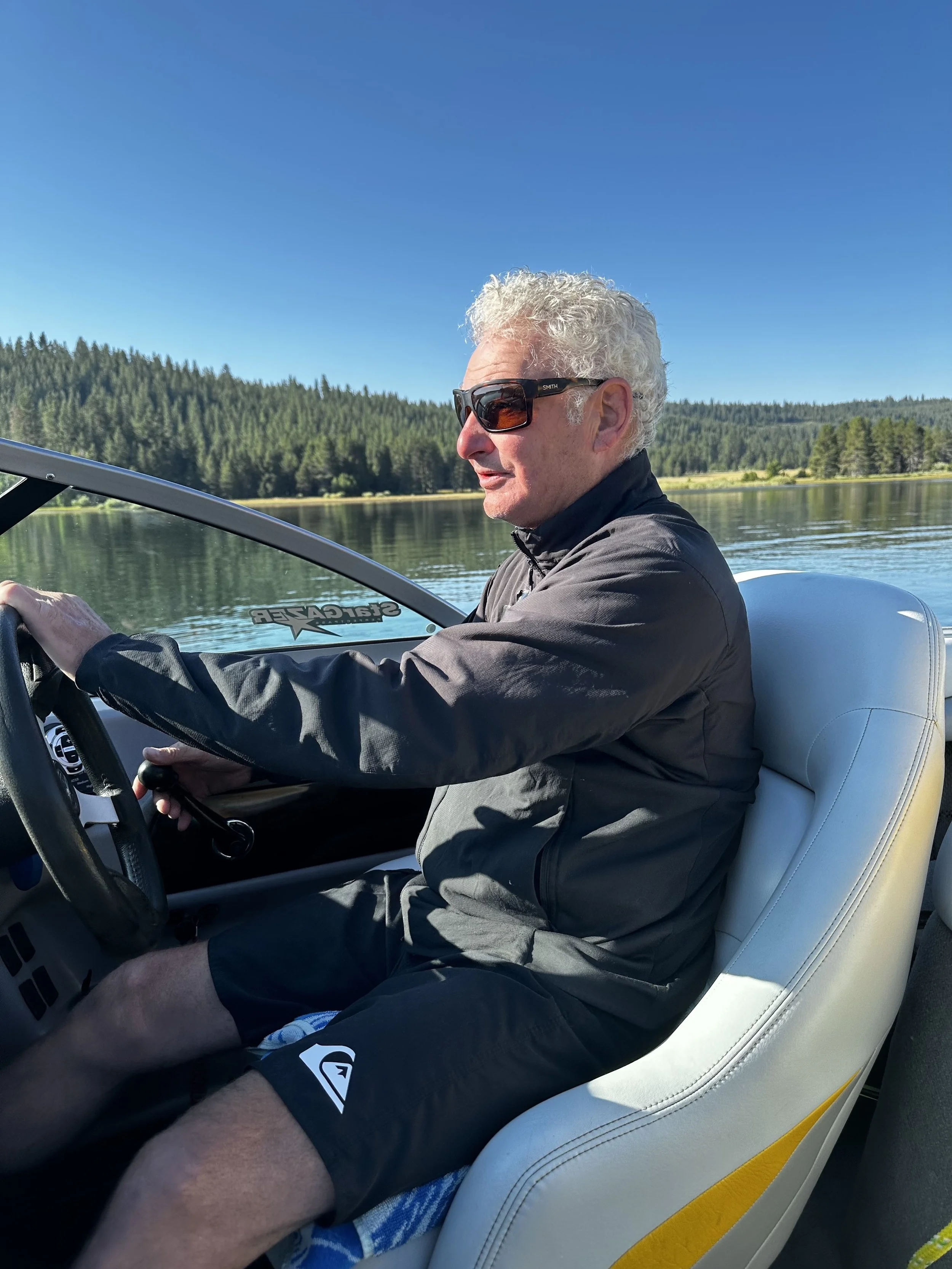 Griff Davis, owner of Griff Davis Construction, at the helm of a boat on a pine-lined mountain lake