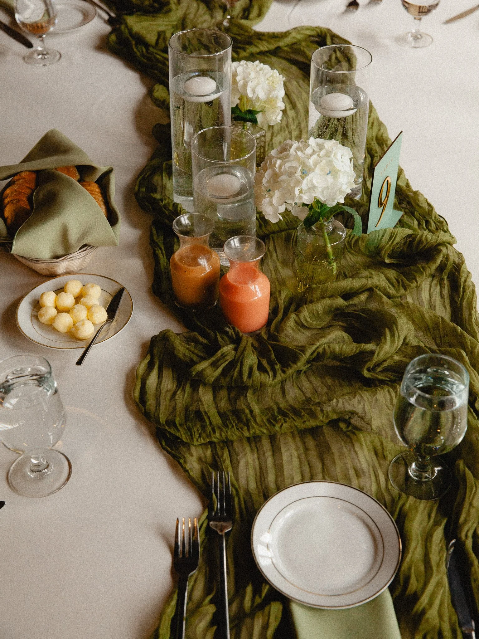 Wedding reception table setting with green linen runner, candles and white flowers