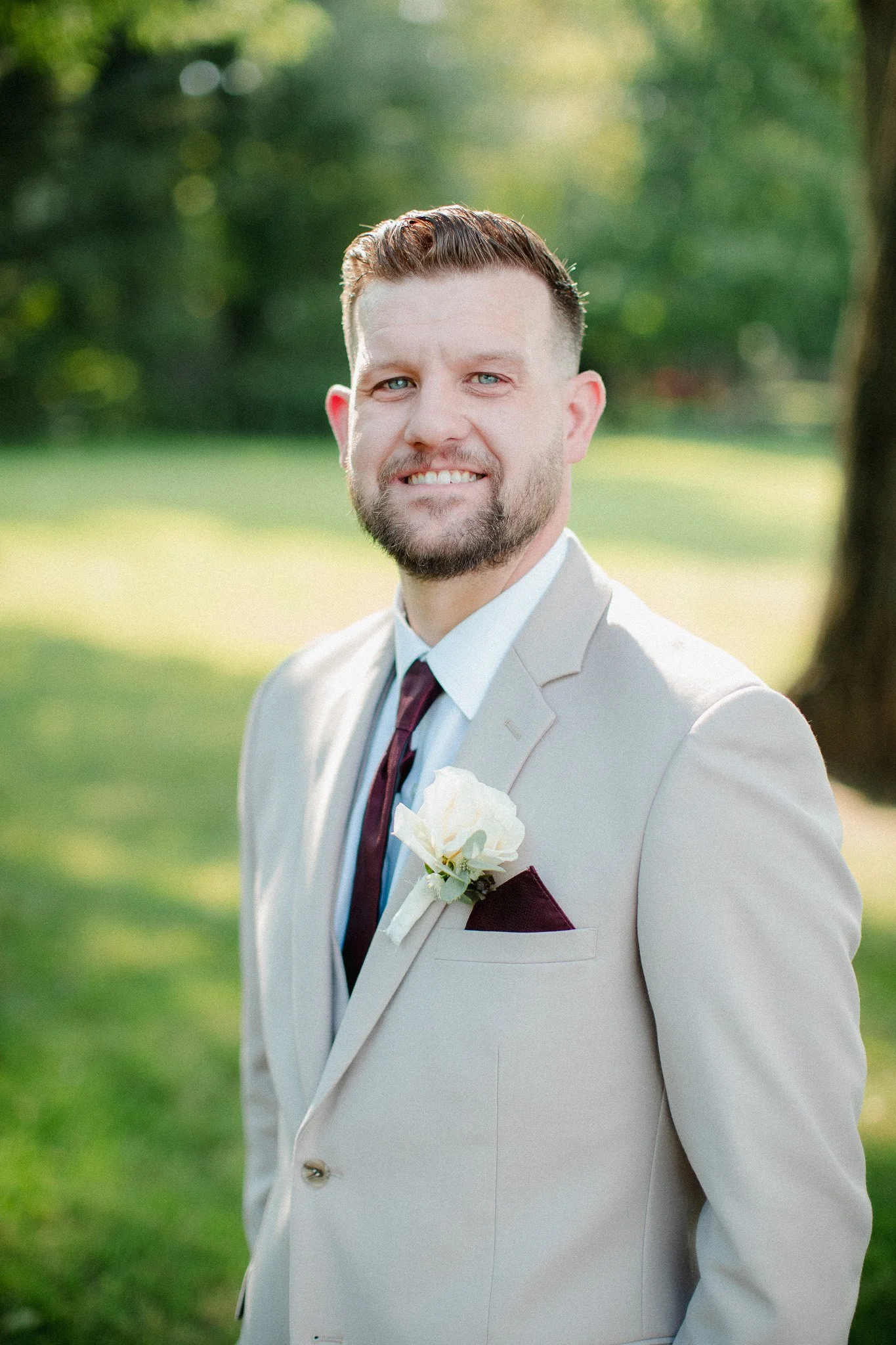 Smiling groom in a light gray suit with a white boutonniere outdoors