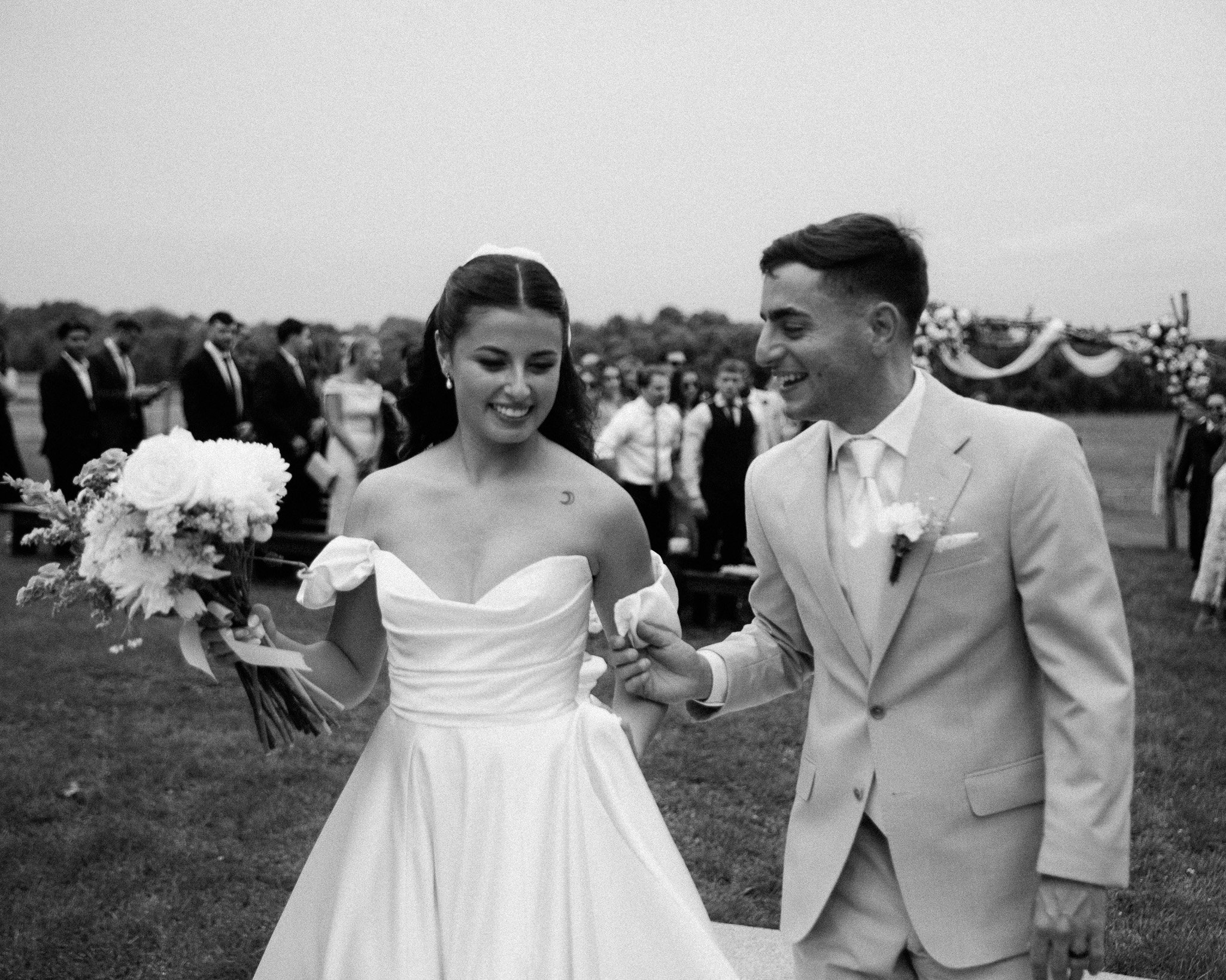 Bride and groom walking back up the aisle as guests cheer, black and white