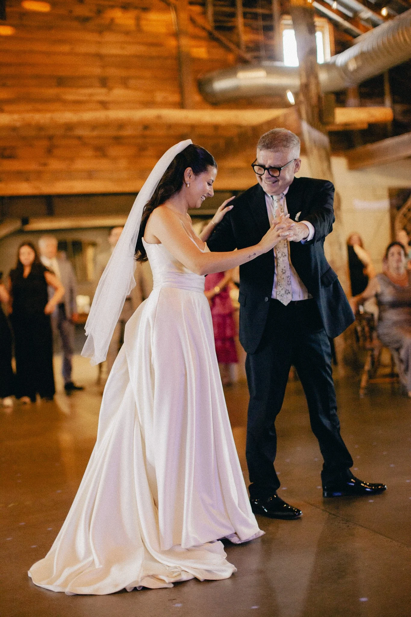 Bride dancing with a guest in a rustic barn reception hall