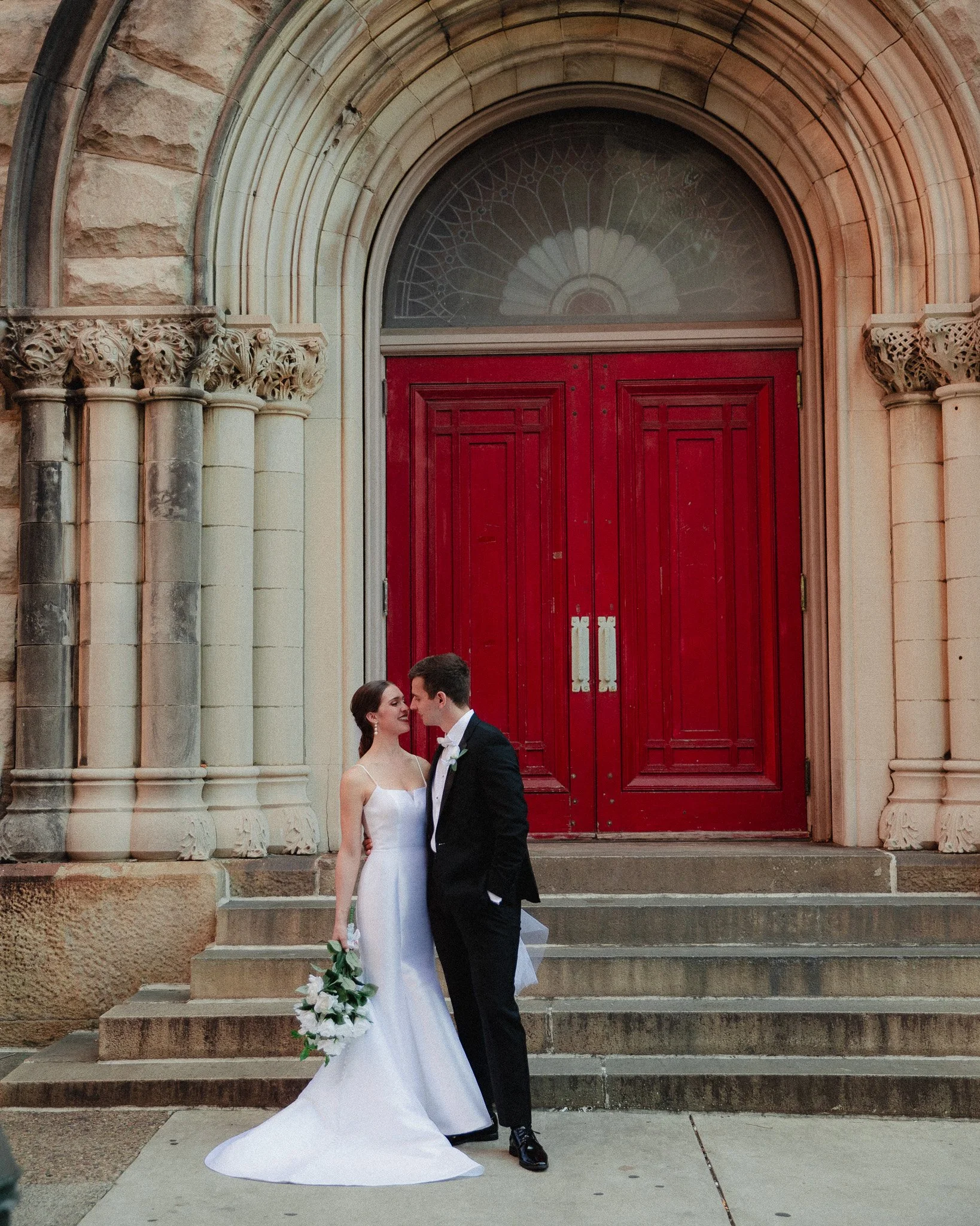 Bride and groom kissing in front of red church doors, East Coast wedding