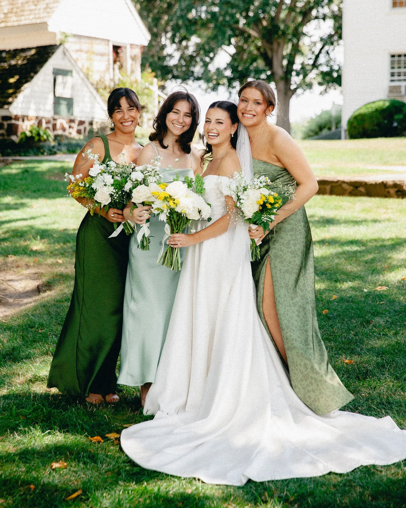 Bride with bridesmaids in sage green dresses holding bouquets on the lawn