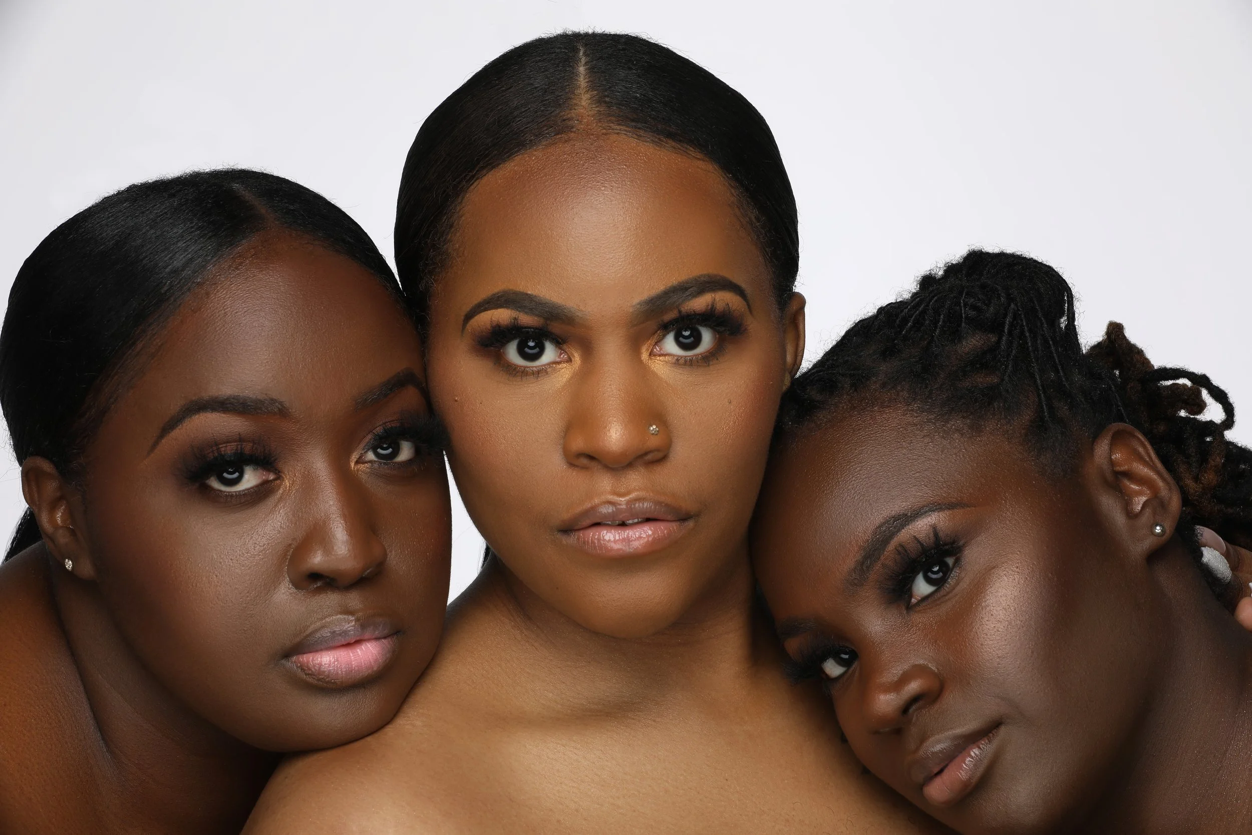 Three women with smooth, glowing skin and elegant makeup, close together against a white background.