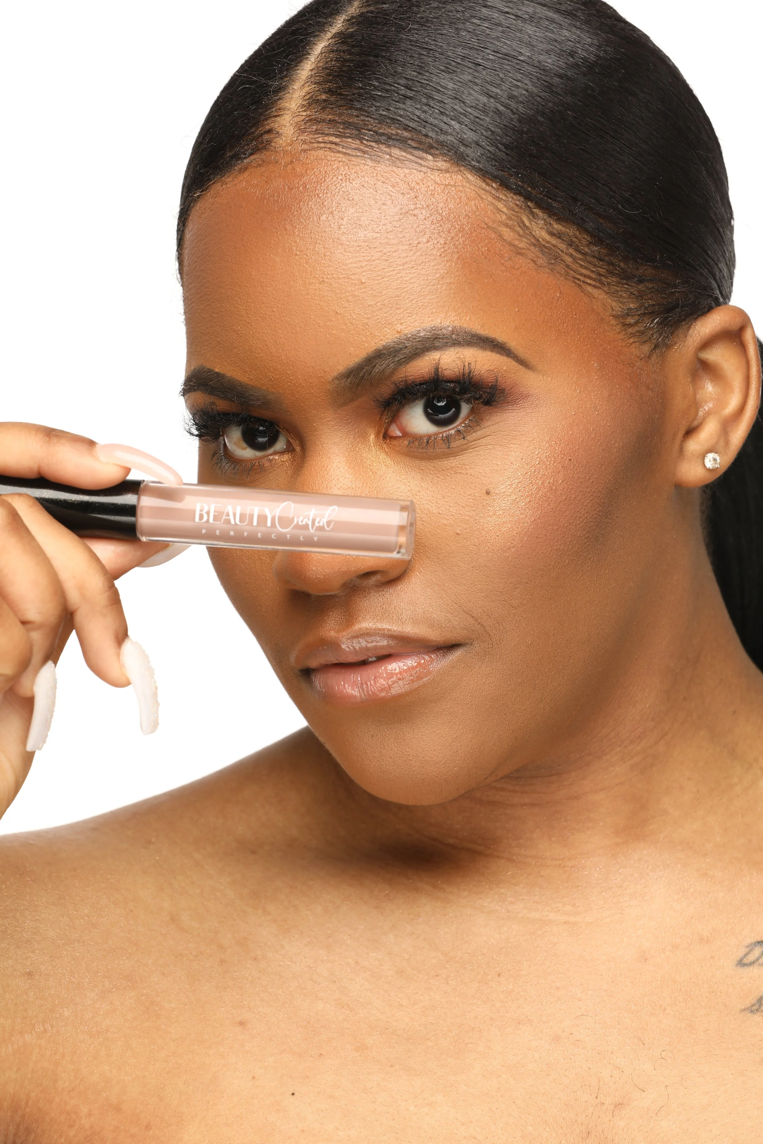 Person holding a tube of lip gloss near their face, with the words 'BEAUTY' visible. The person has a neutral expression and styled hair.