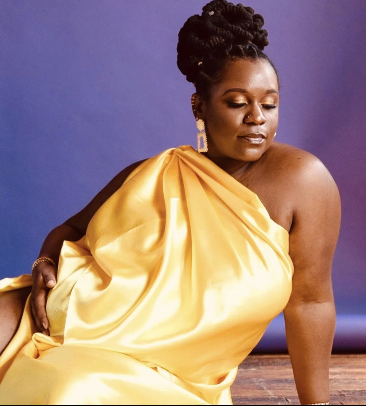 Person wearing a yellow satin dress against a purple background