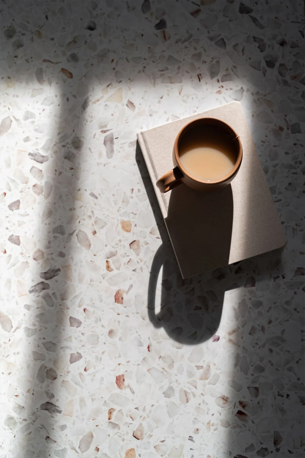 Overhead view of coffee cup on notebook in natural light, representing thoughtful, focused work environment