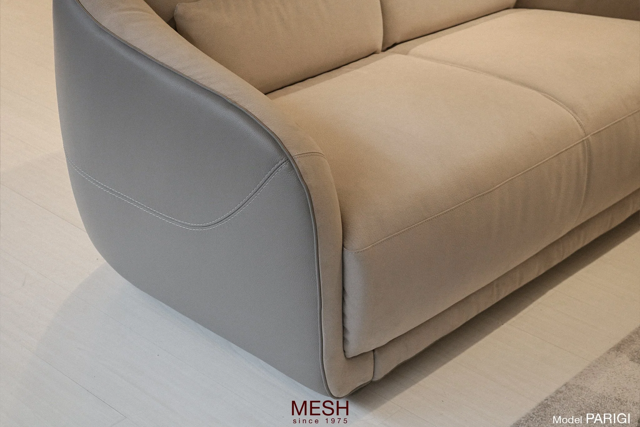 Close-up van een beige bank met een armleuning bekleed met grijs kunstleder en een beige stoffering op de zitting en rugleuning.