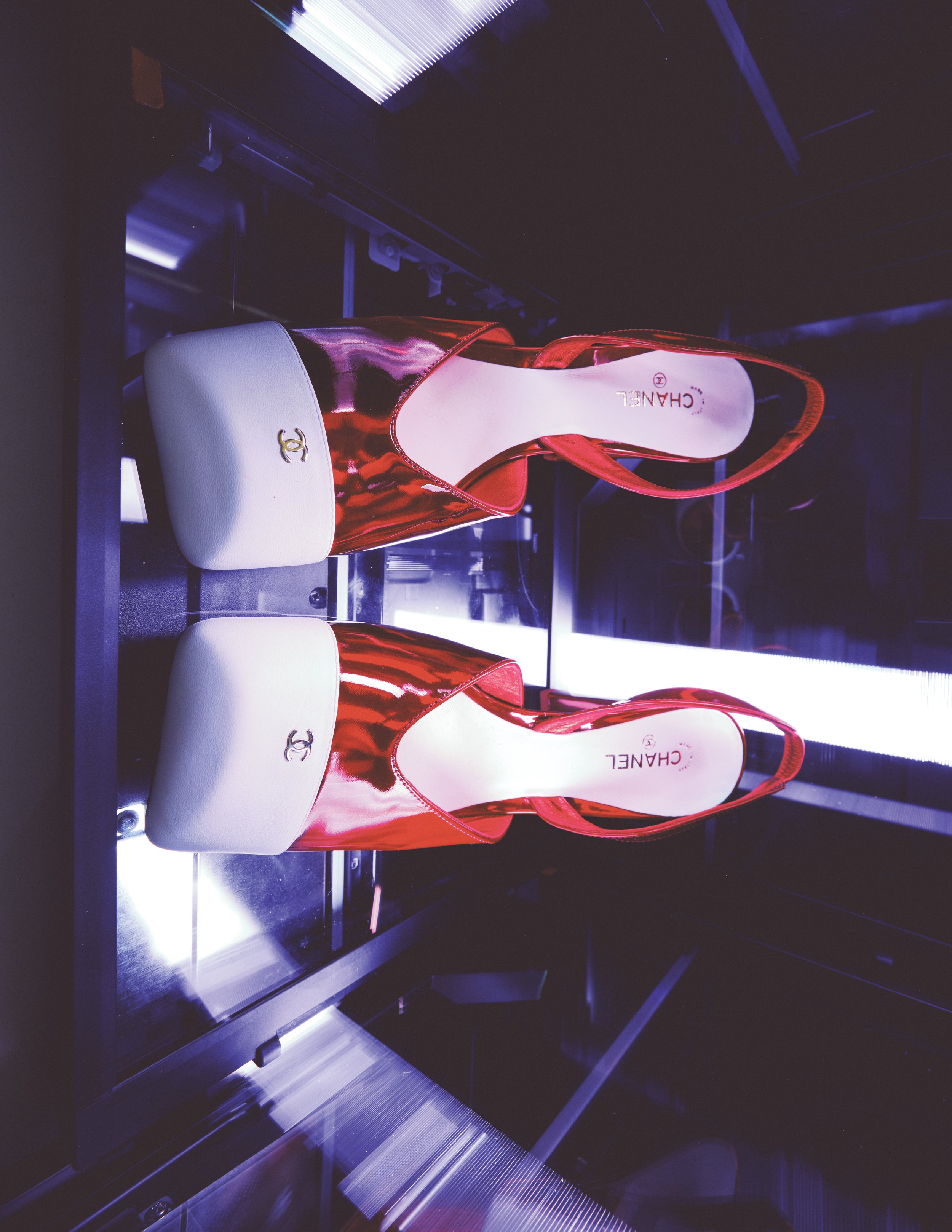 Red and white Chanel high-heeled shoes in a glass display case with lighting.
