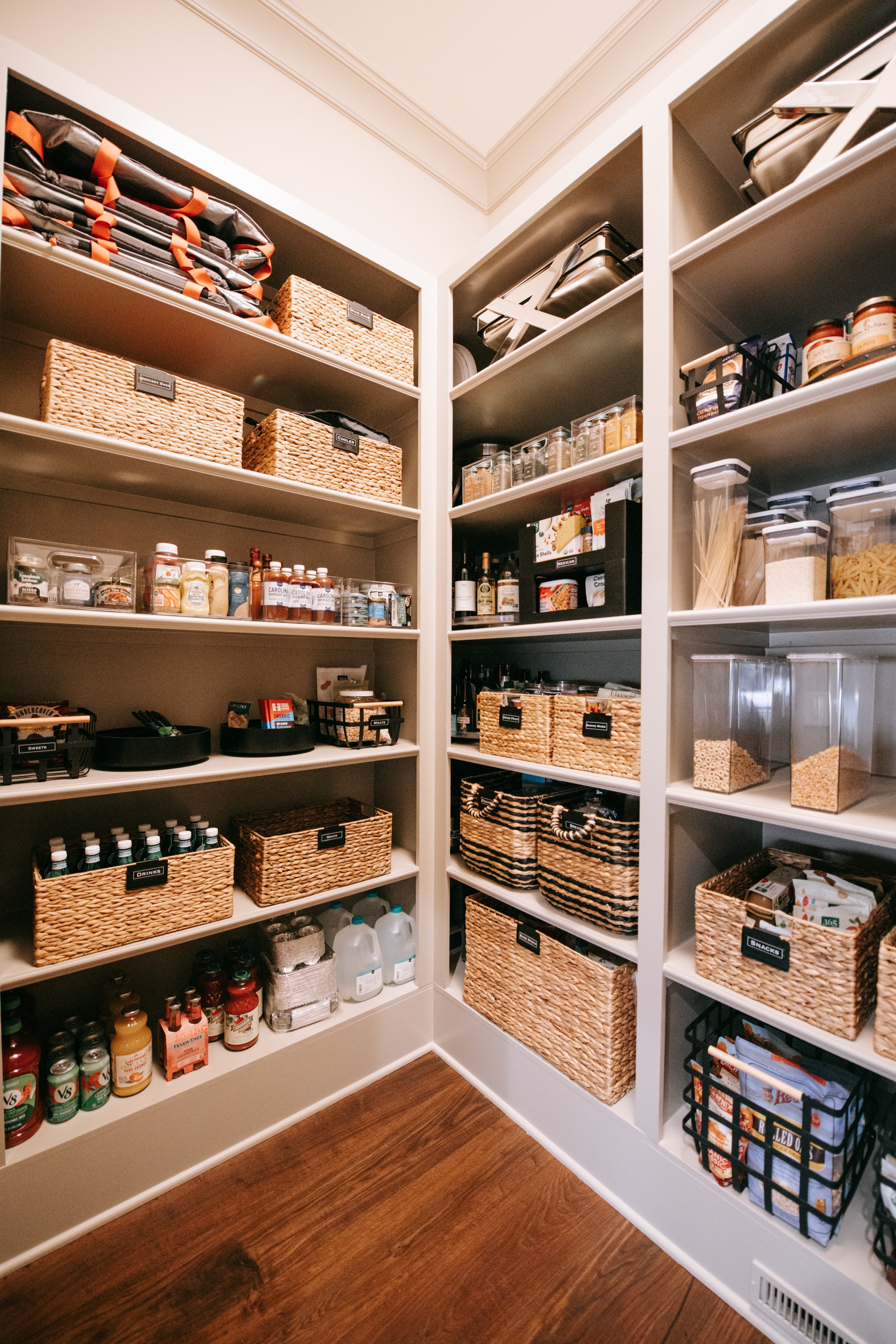 Well-organized pantry with woven baskets, shelves with spices, grains, and canned goods, and neatly stored kitchen supplies.