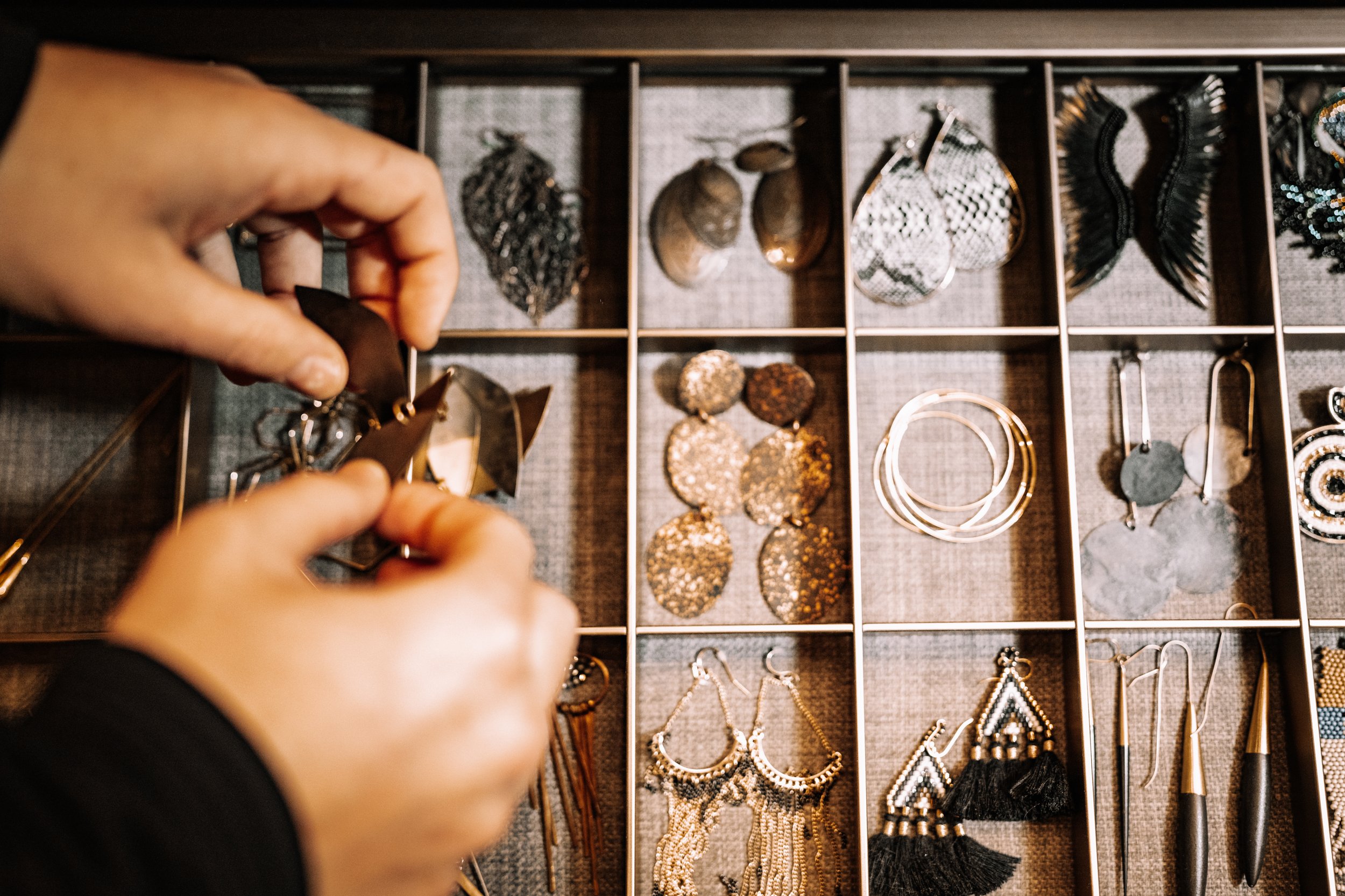 Hands sorting earrings in a jewelry organizer with various styles and colors.
