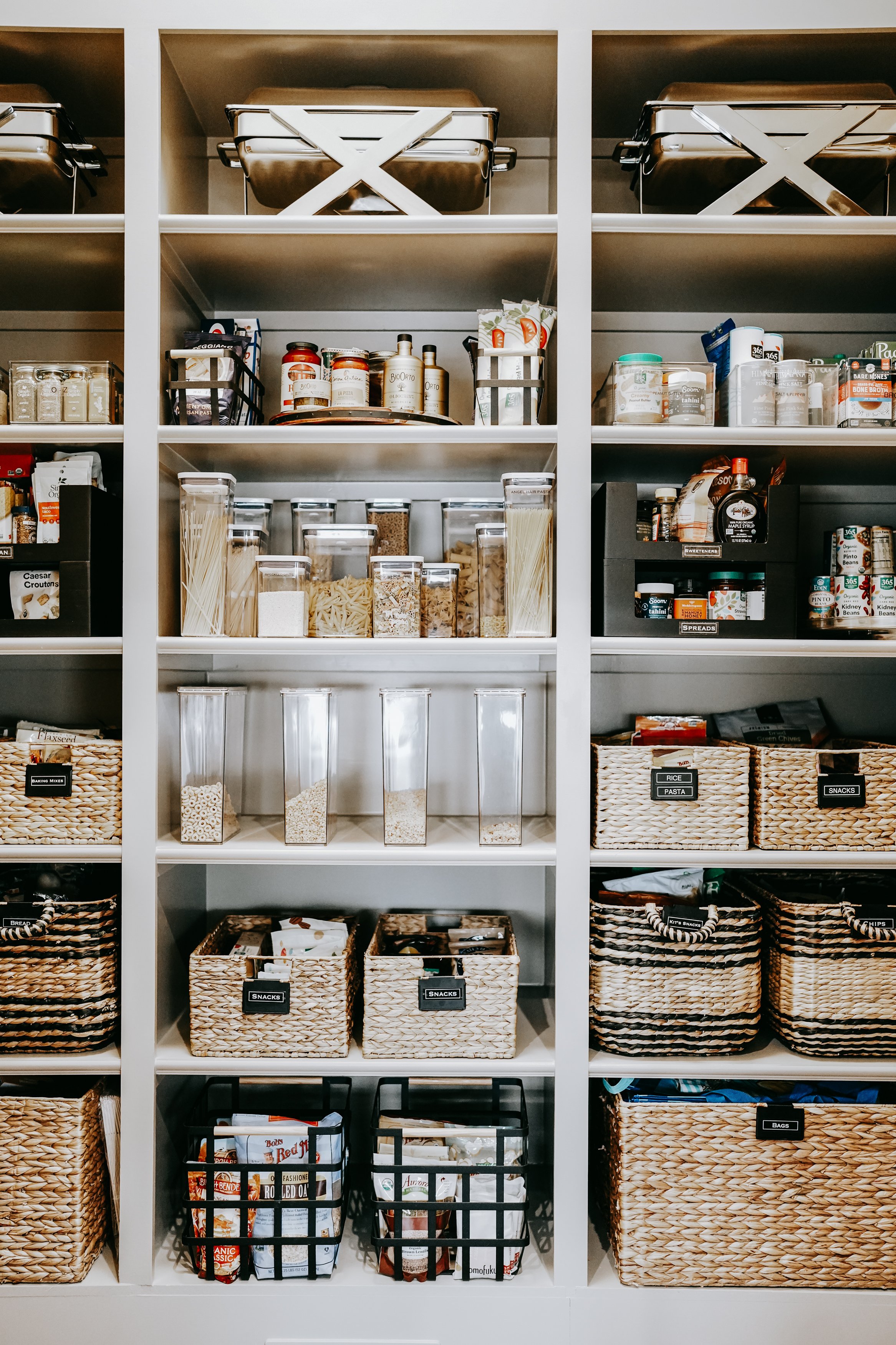 Organized pantry with labeled baskets, jars of pasta, cereal containers, canned goods, and jars.