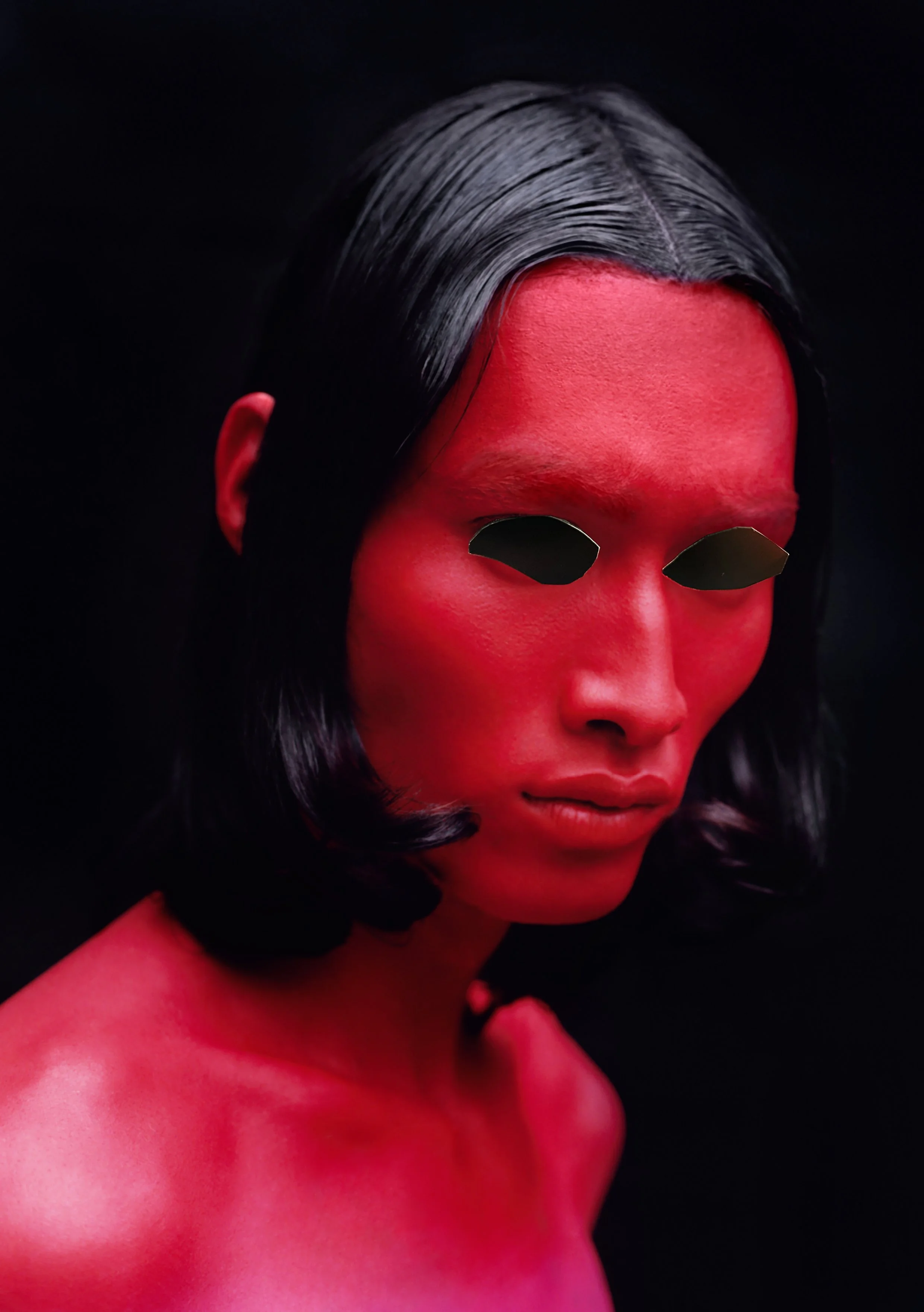 A person with long black hair and skin painted red against a black background, with blacked-out eyes.