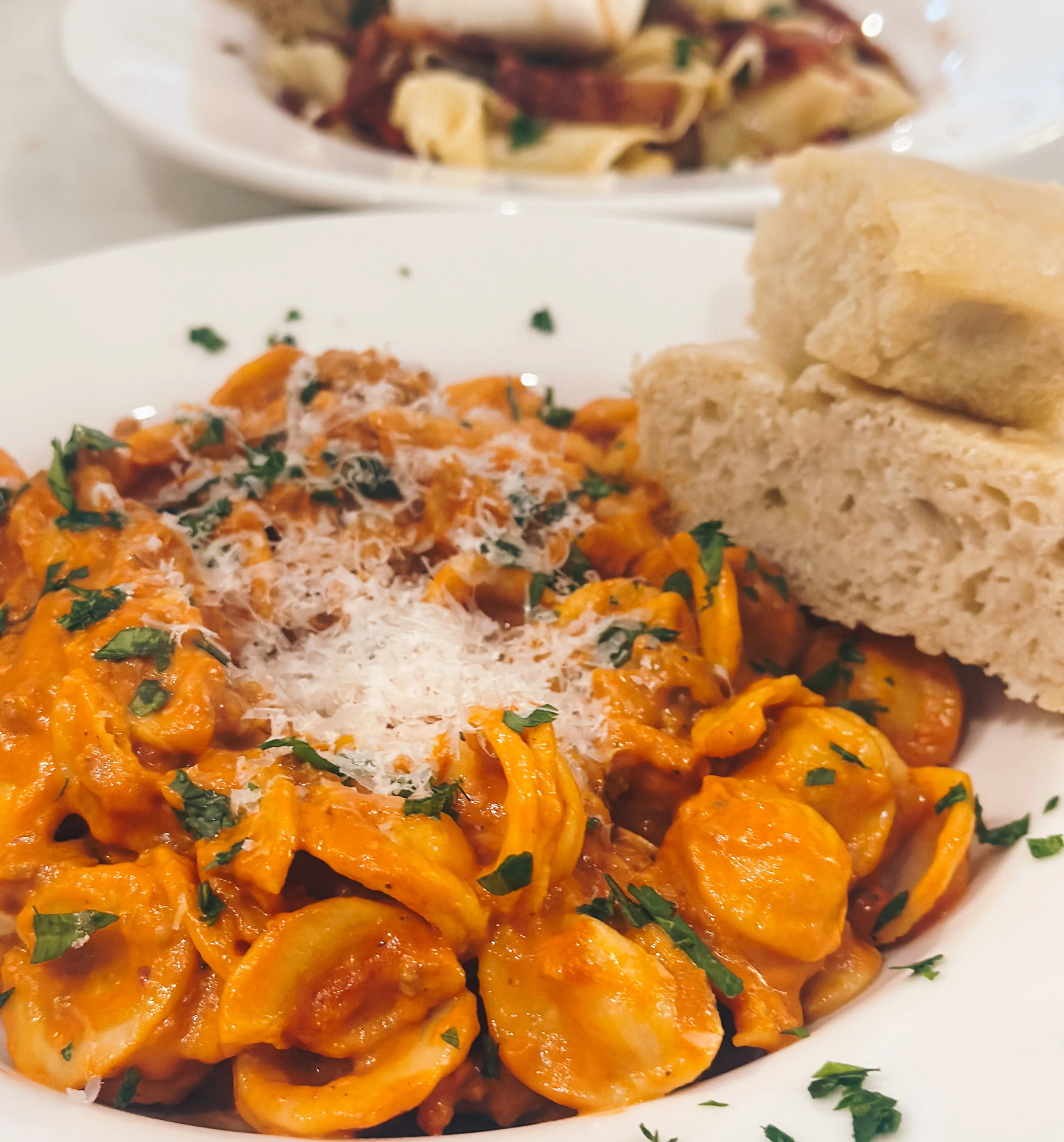 A plate of chicken and sausage jambalaya garnished with parsley, served with two pieces of bread, and a bowl of pasta salad in the background.