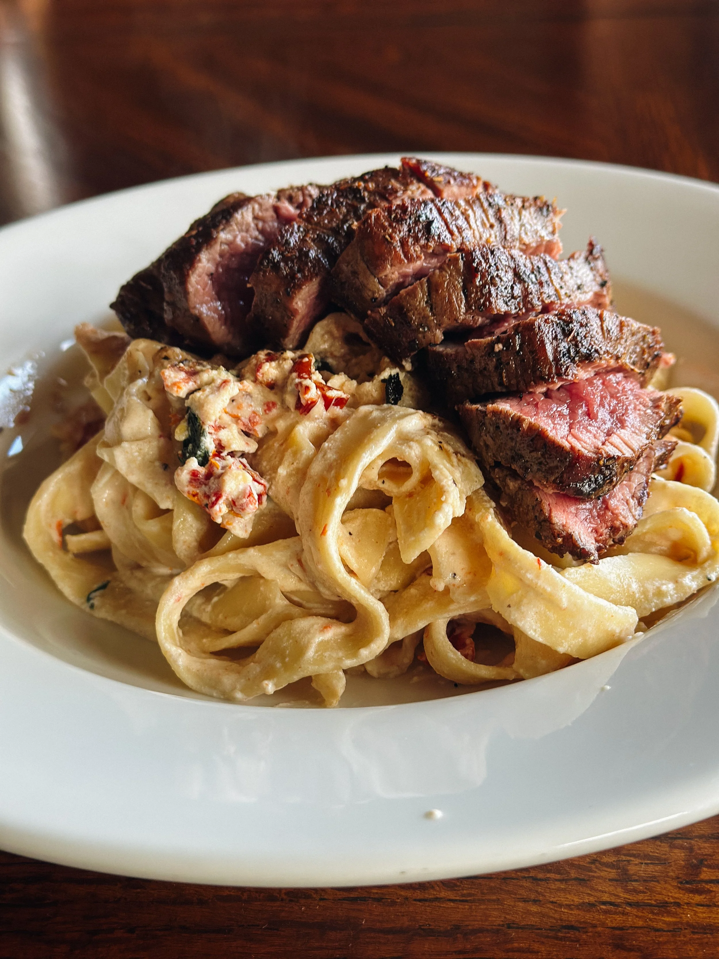 A plate of cooked pasta with creamy sauce and a side of sliced grilled steak.