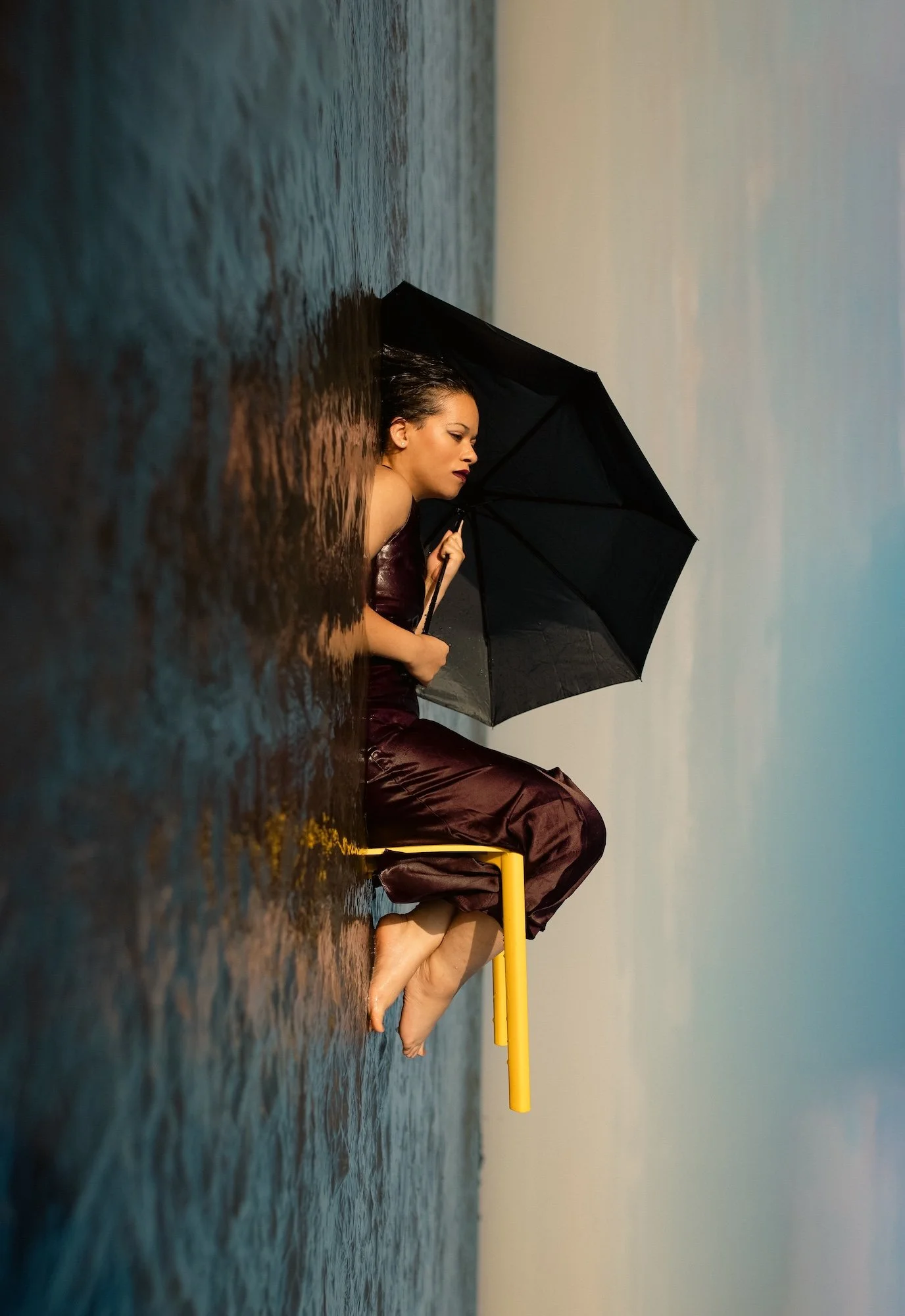 Photographie conceptuelle d’un corps contraint par un angle droit contre un mur, tenant un parapluie dans un espace restreint