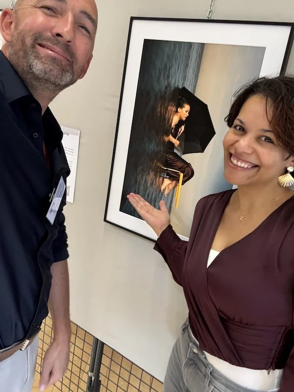 Le photographe François Mougel pose en selfie aux côtés d'Élodie désignant son portrait encadré Quatre-vingt-dix pendant l'exposition.
