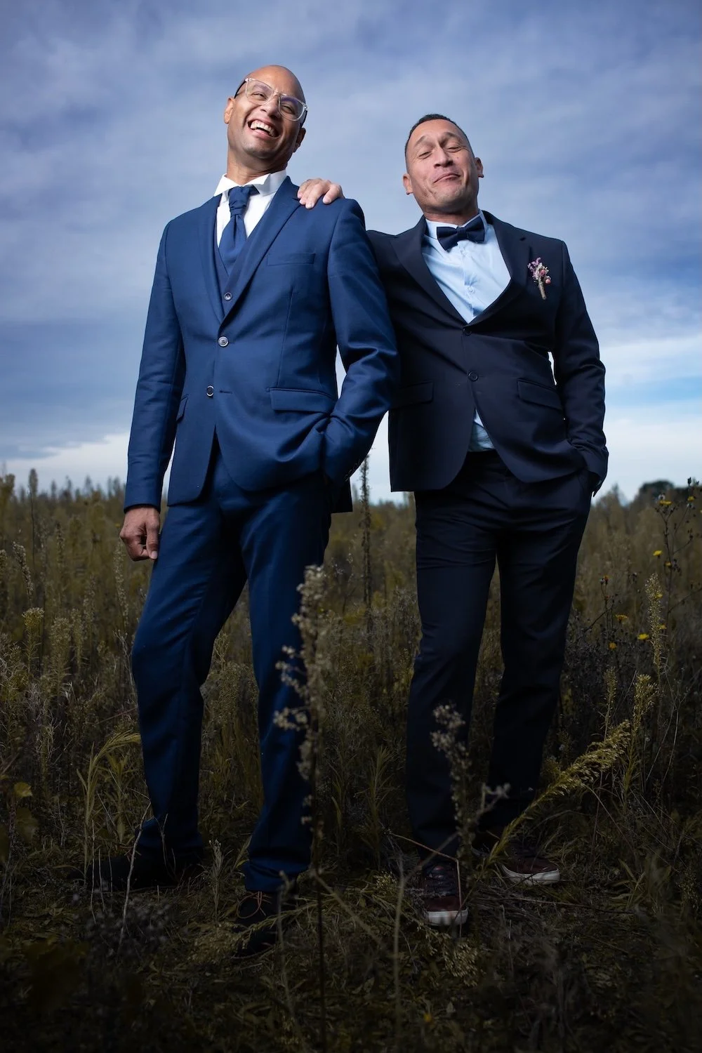 Marié et son témoin rigolant en costume bleu dans un champ à Nantes, photo de mariage spontanée.