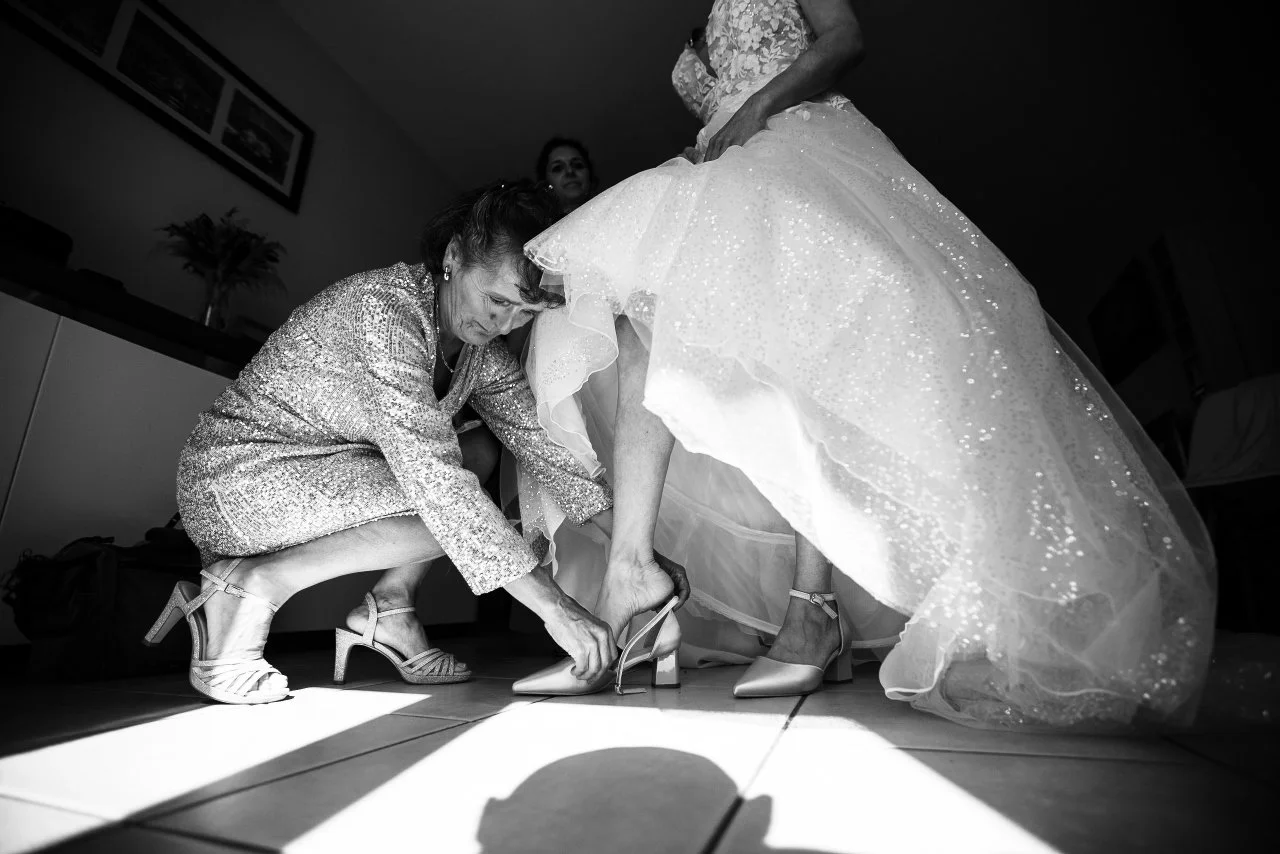 La maman de la mariée lui passe son soulier lors des préparatifs.