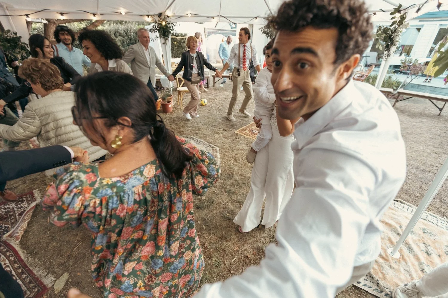 Groupe d'invités dansant en ronde sous une tente lors d'une soirée de mariage juif.