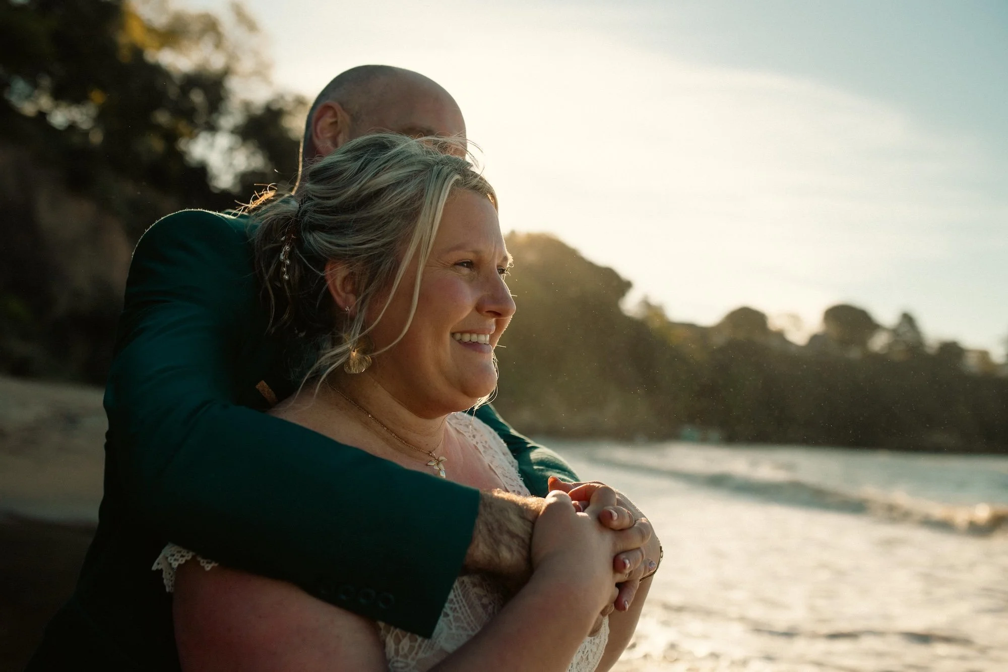 mariée enlacée par son marie qui sourit sur la plage