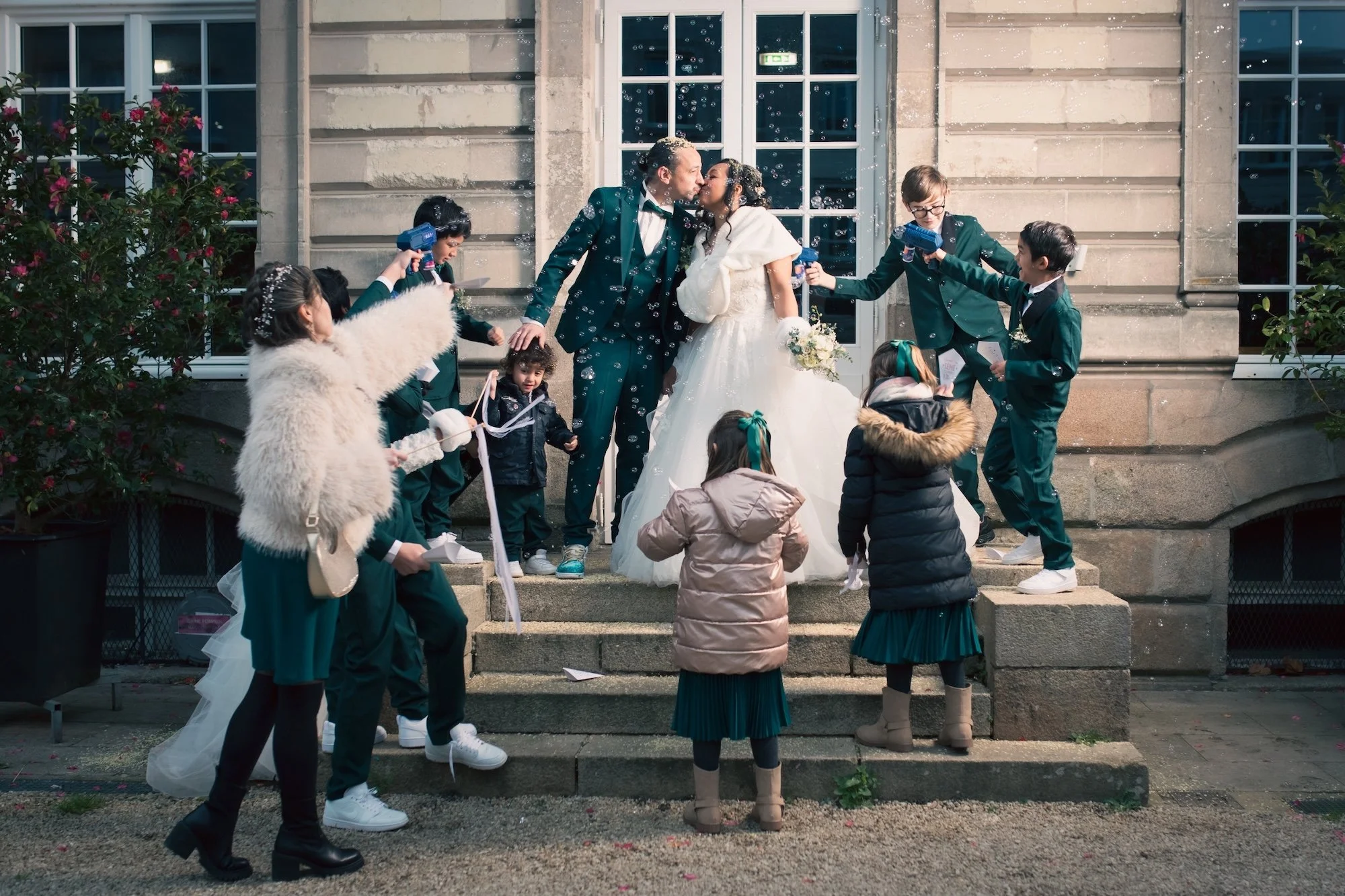 les mariés d'embrassent pendant que leurs enfants jettent des cotillons devant un chateau en pays de Loire